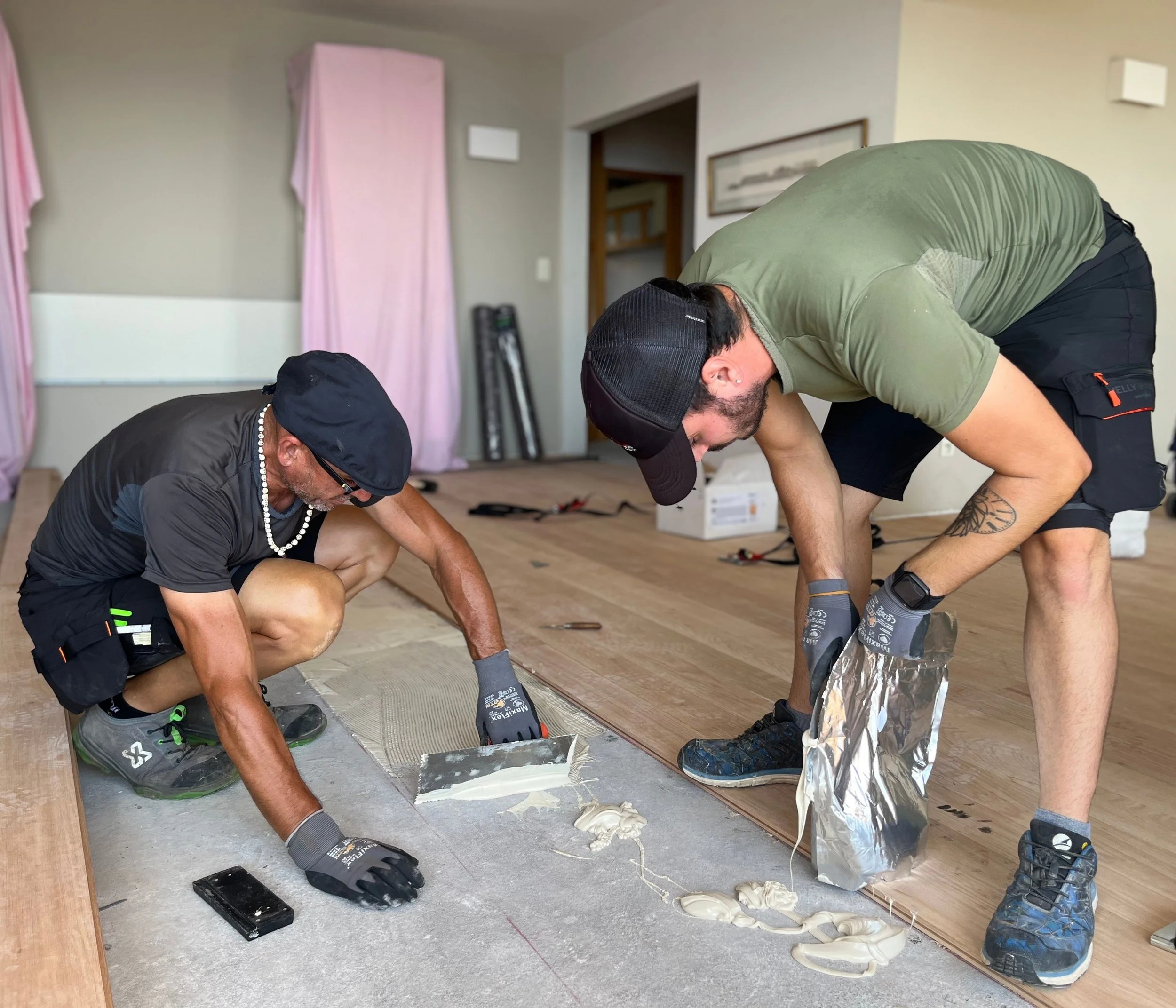 Deux hommes posant du parquet en déposant de la colle au sol. 