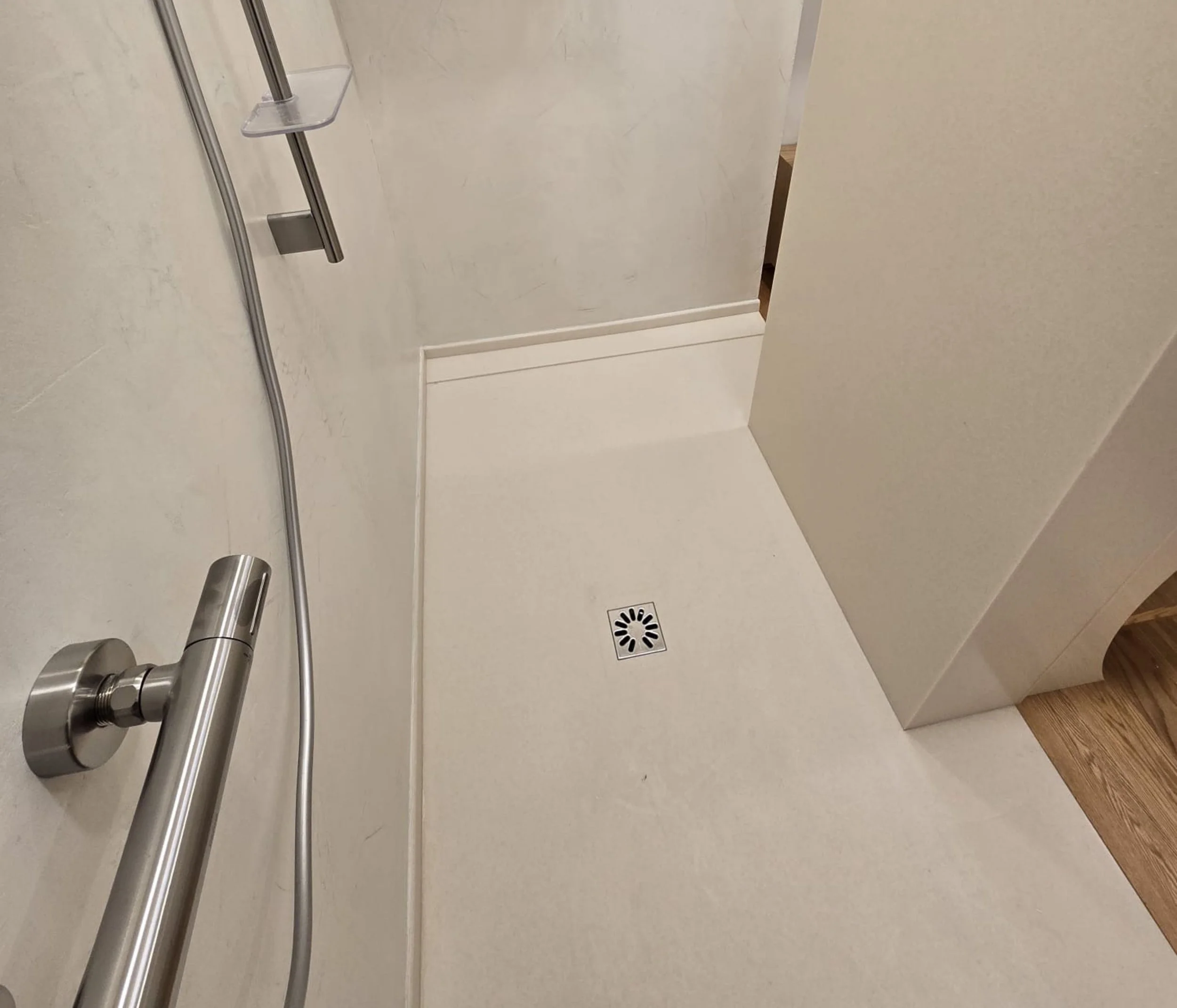 Vue d'un bac à douche en corian avec un pommeau, un tapis de sol à drain central, murs en beige clair, et un sol en bois.