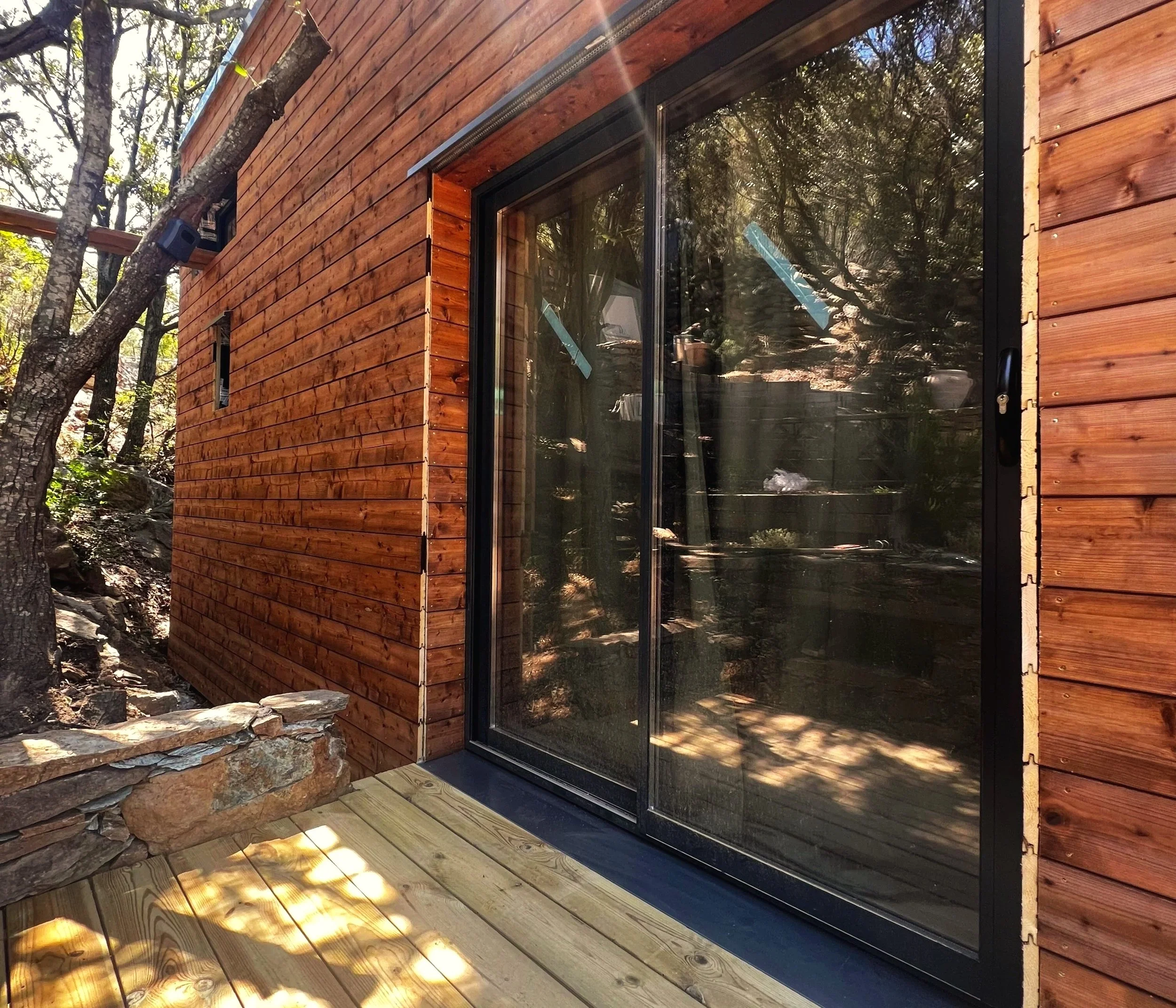 Maison ossature bois avec façade vitrée, intégrée dans un environnement naturel.