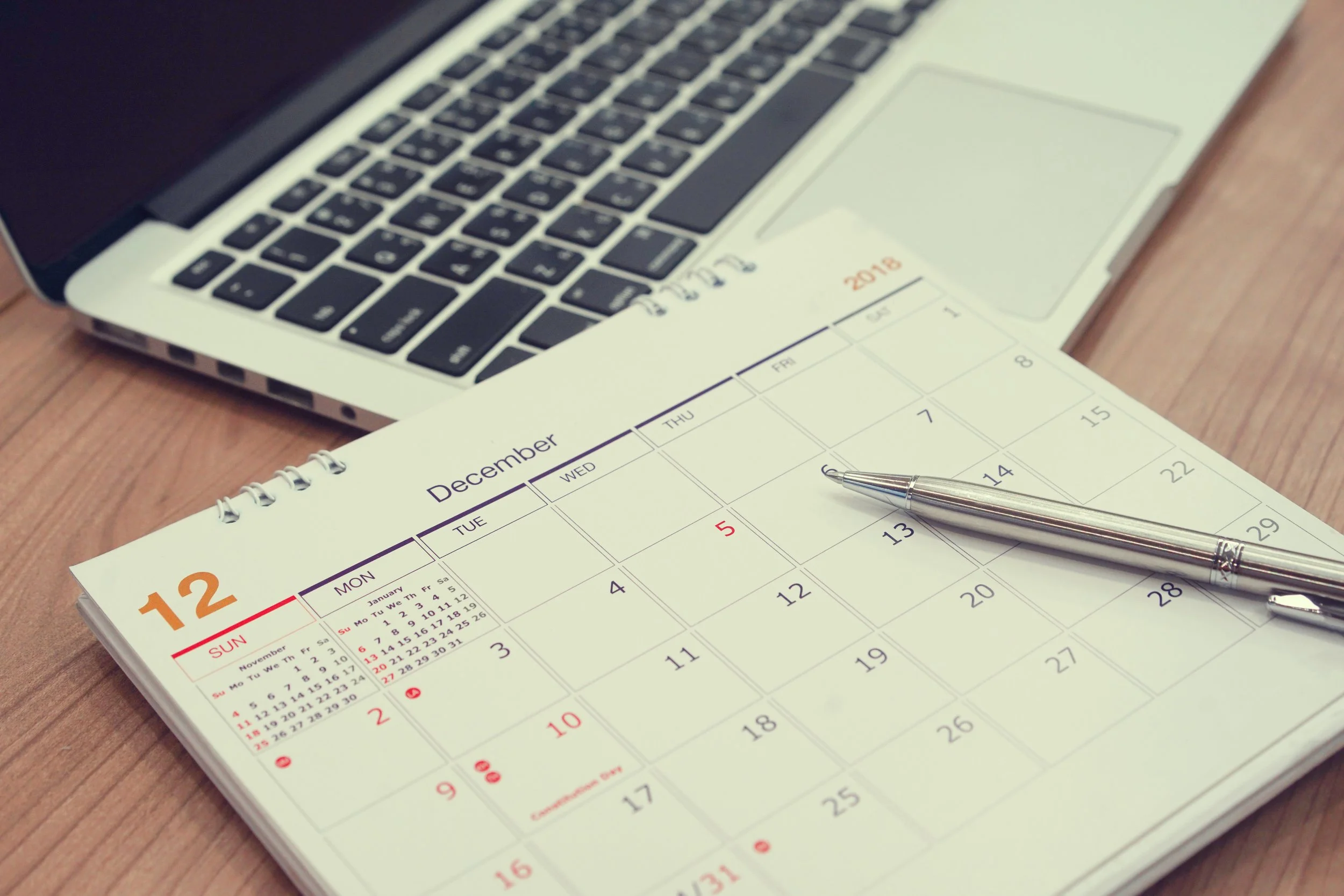 Close-up of a December 2018 calendar with pen and laptop on a desk.