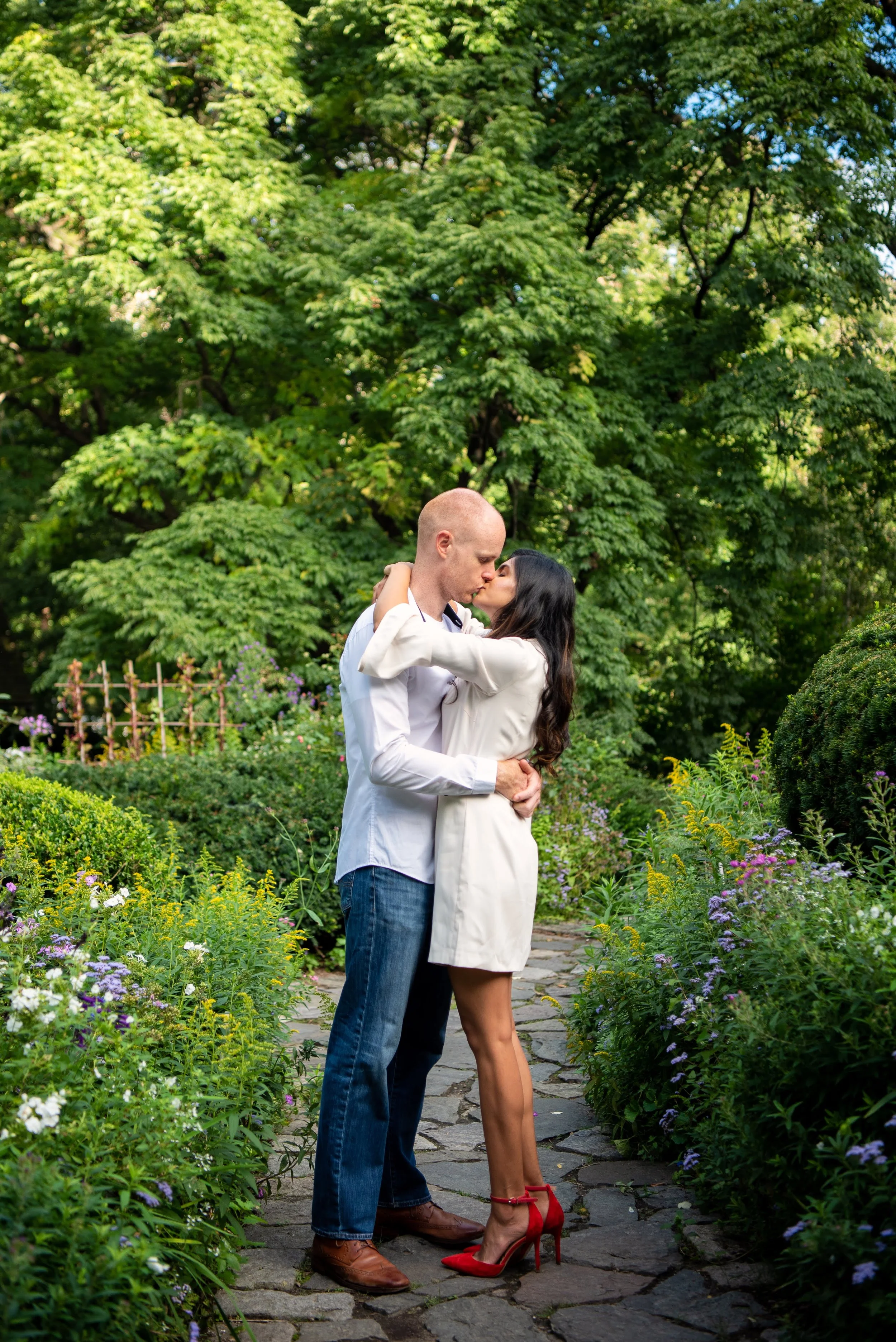 A couple kissing while standing on a path in the Shakespeare Garden in Central Park