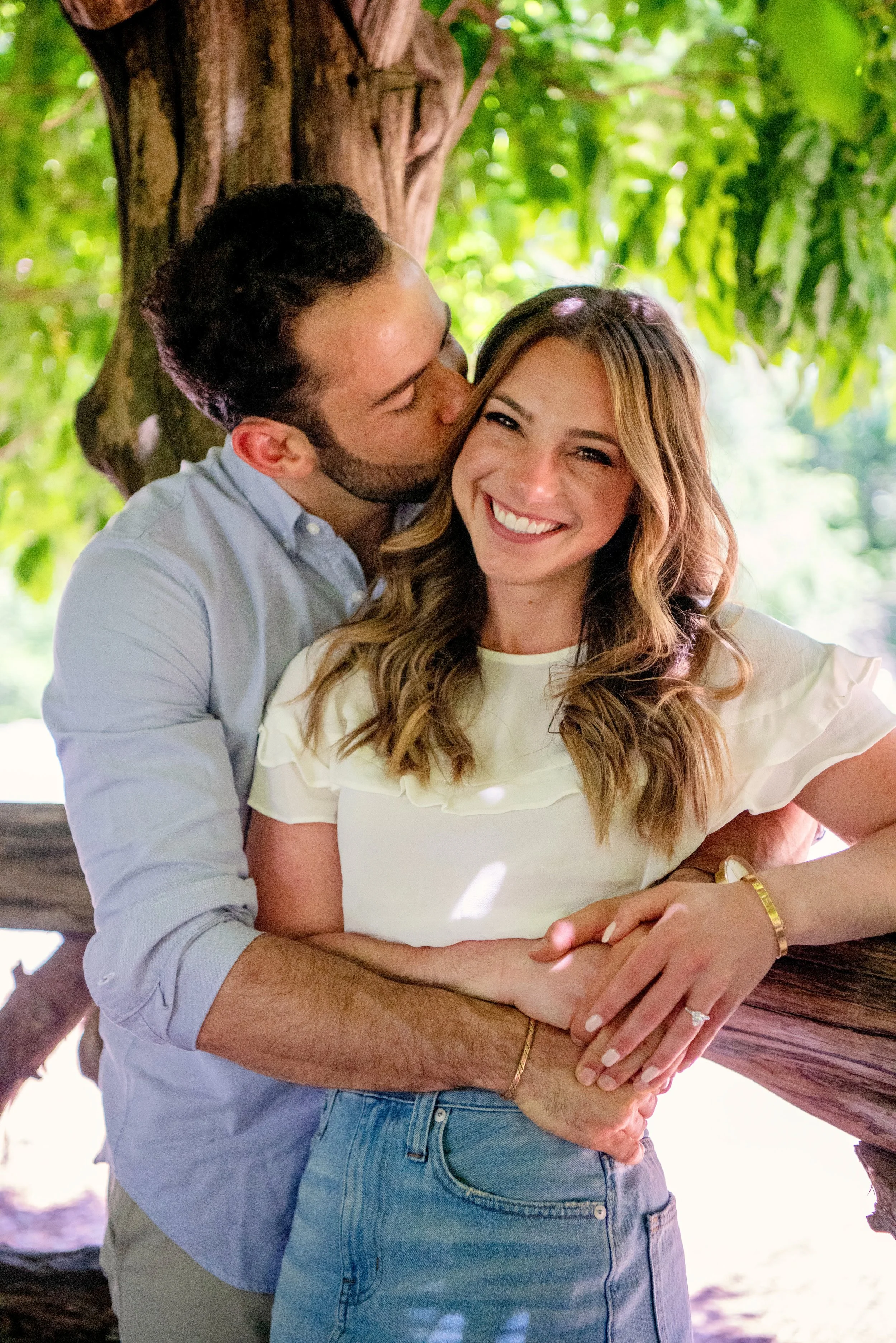 A waist-up image of a man hugging his new fiancée from behind at the Cop Cot in Central Park