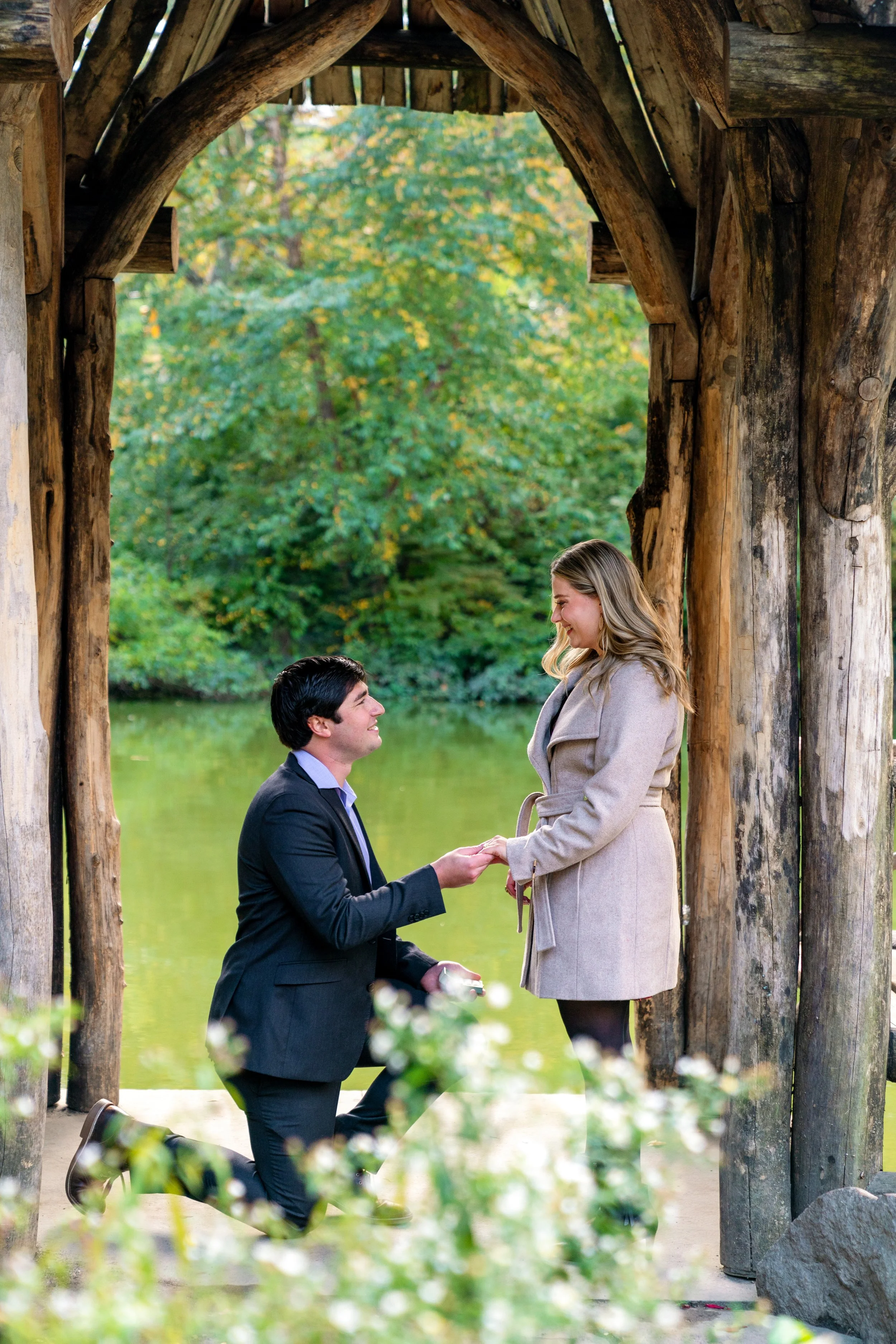 A man on one knee, proposing to his girlfriend, at Wagner Cove in Central Park