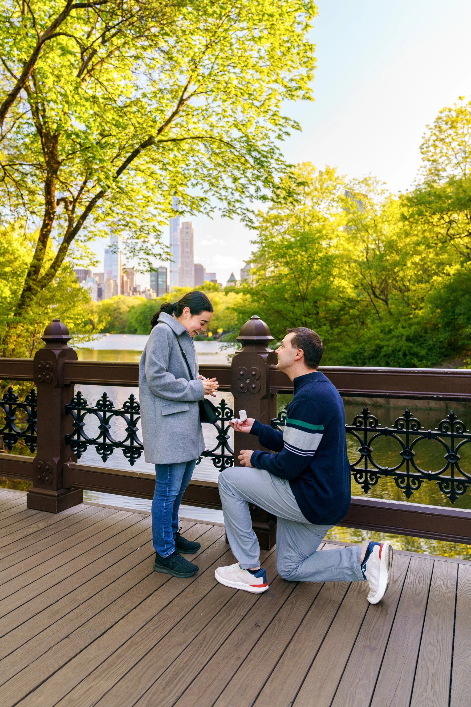 Man proposing on the Oak Bridge in Central Park with the lake and skyline in the background