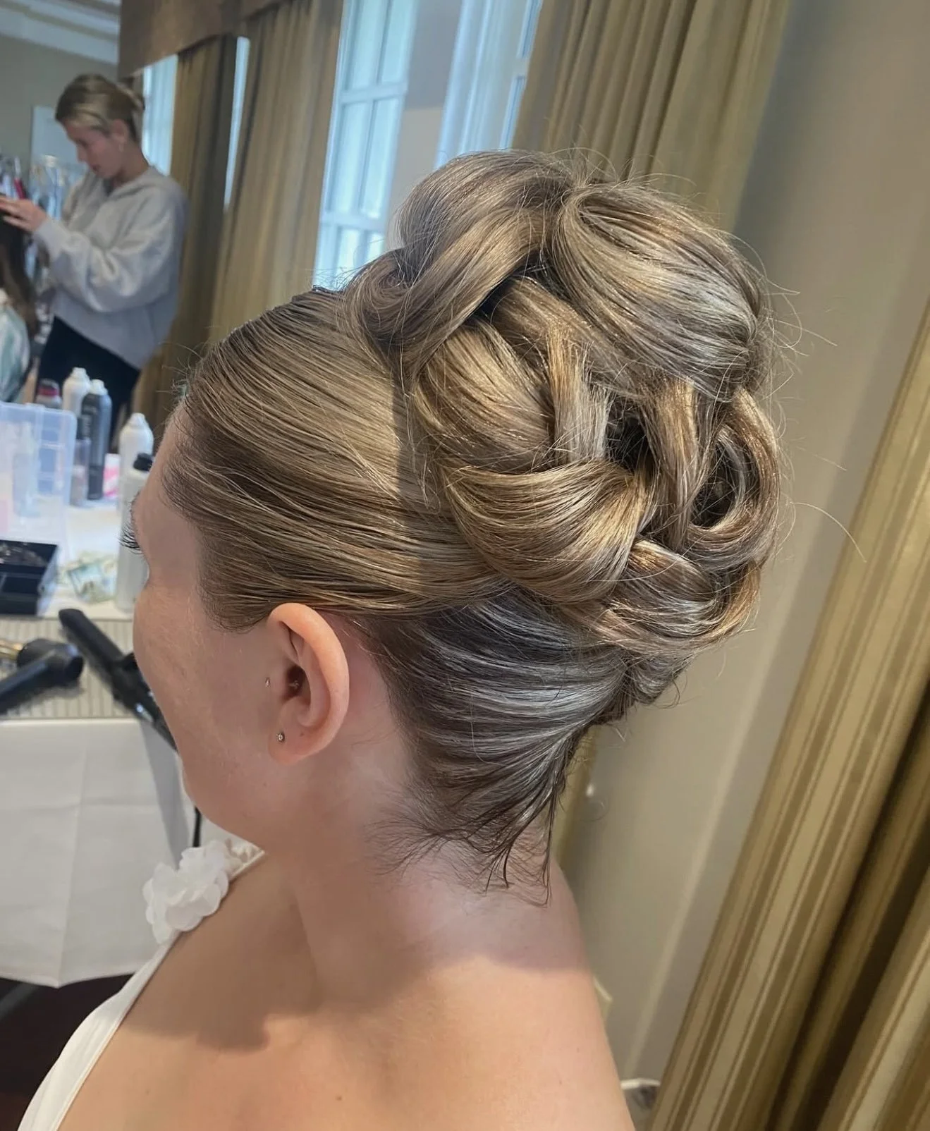 Updo hairstyle with intricate braids and twists on a blonde woman, preparing for a special event or occasion.