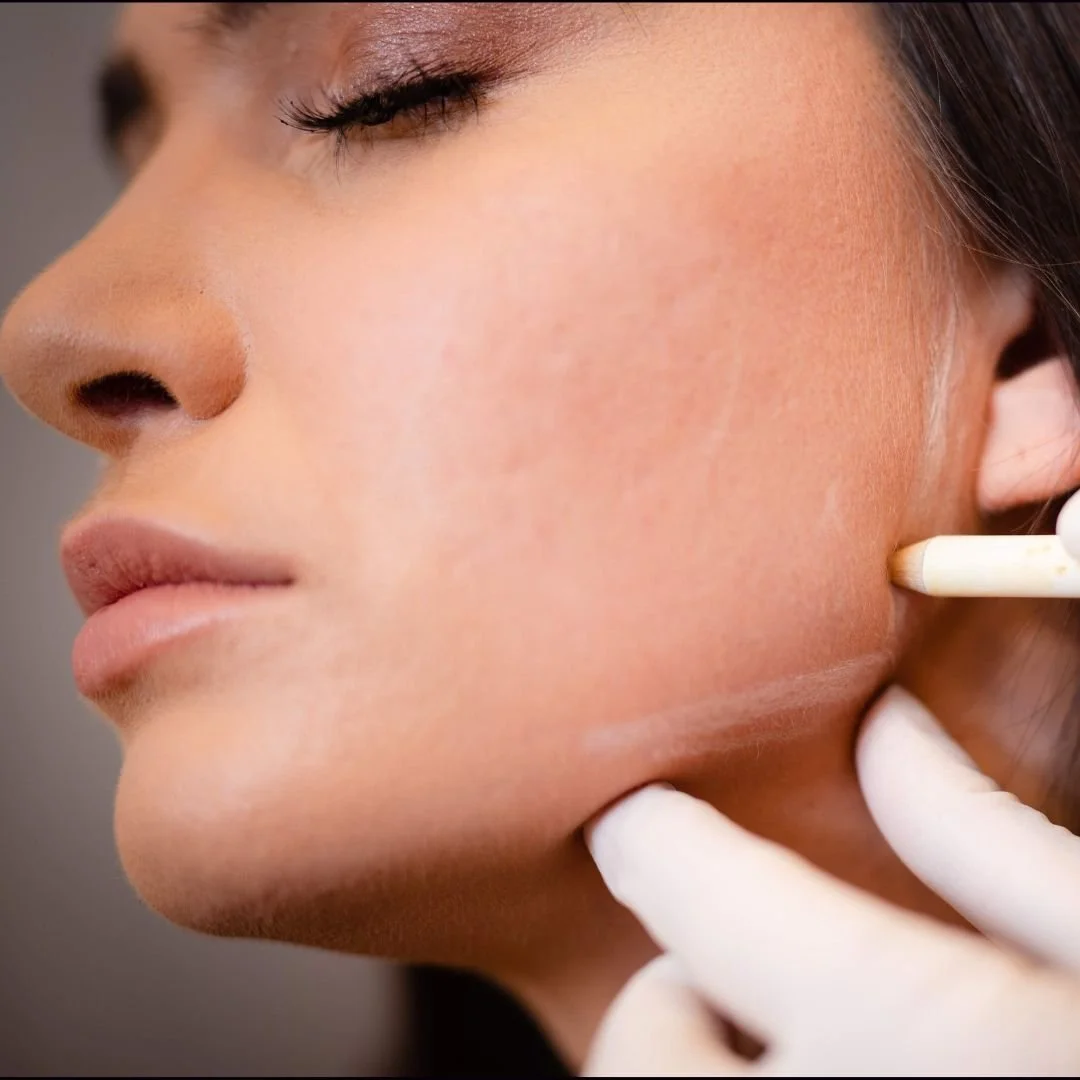 Close-up of a woman's face with her eyes closed as a gloved hand examines her jawline with a tool.