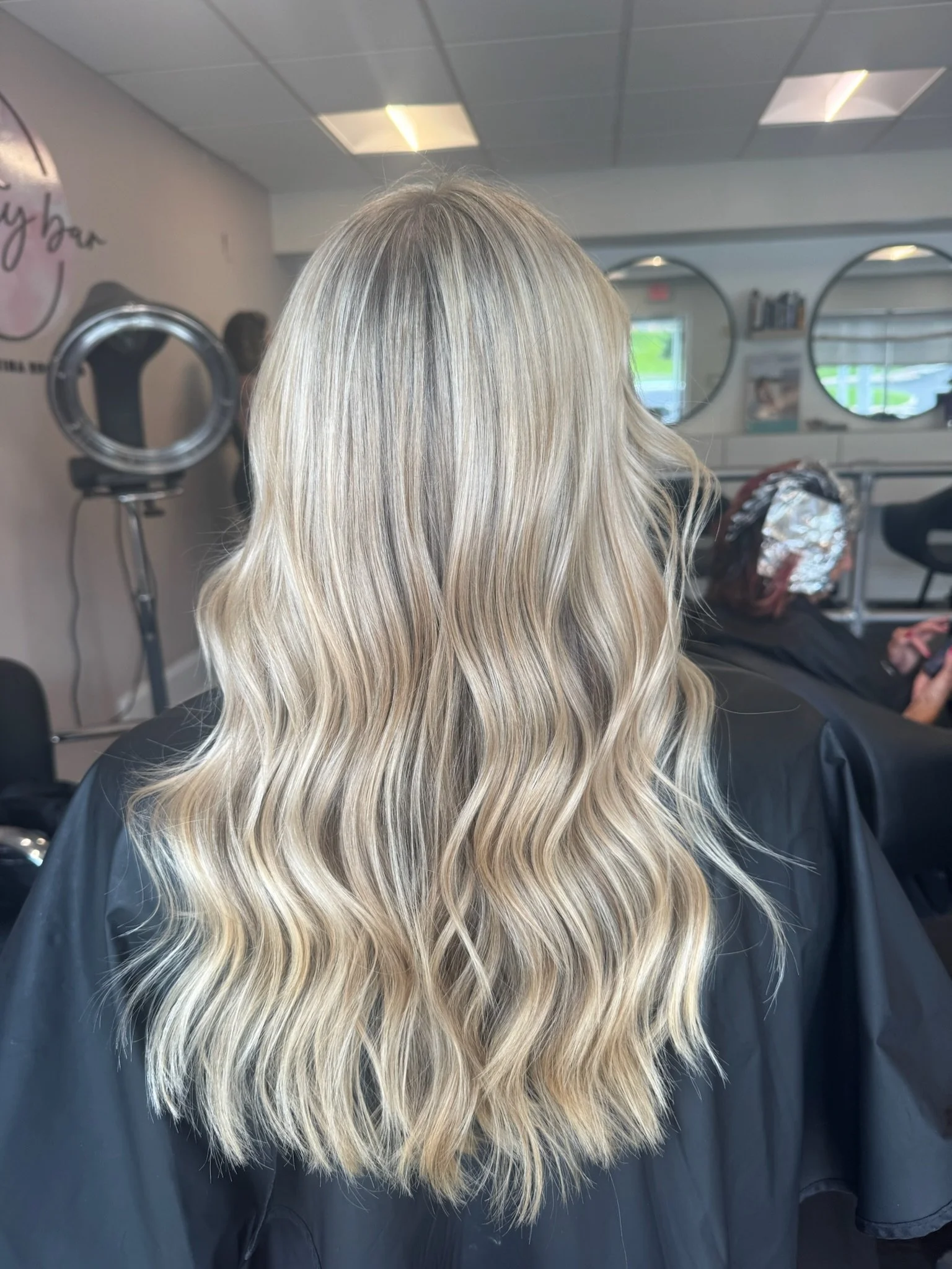 Blonde woman with wavy hair sitting in a salon chair inside a hair salon.
