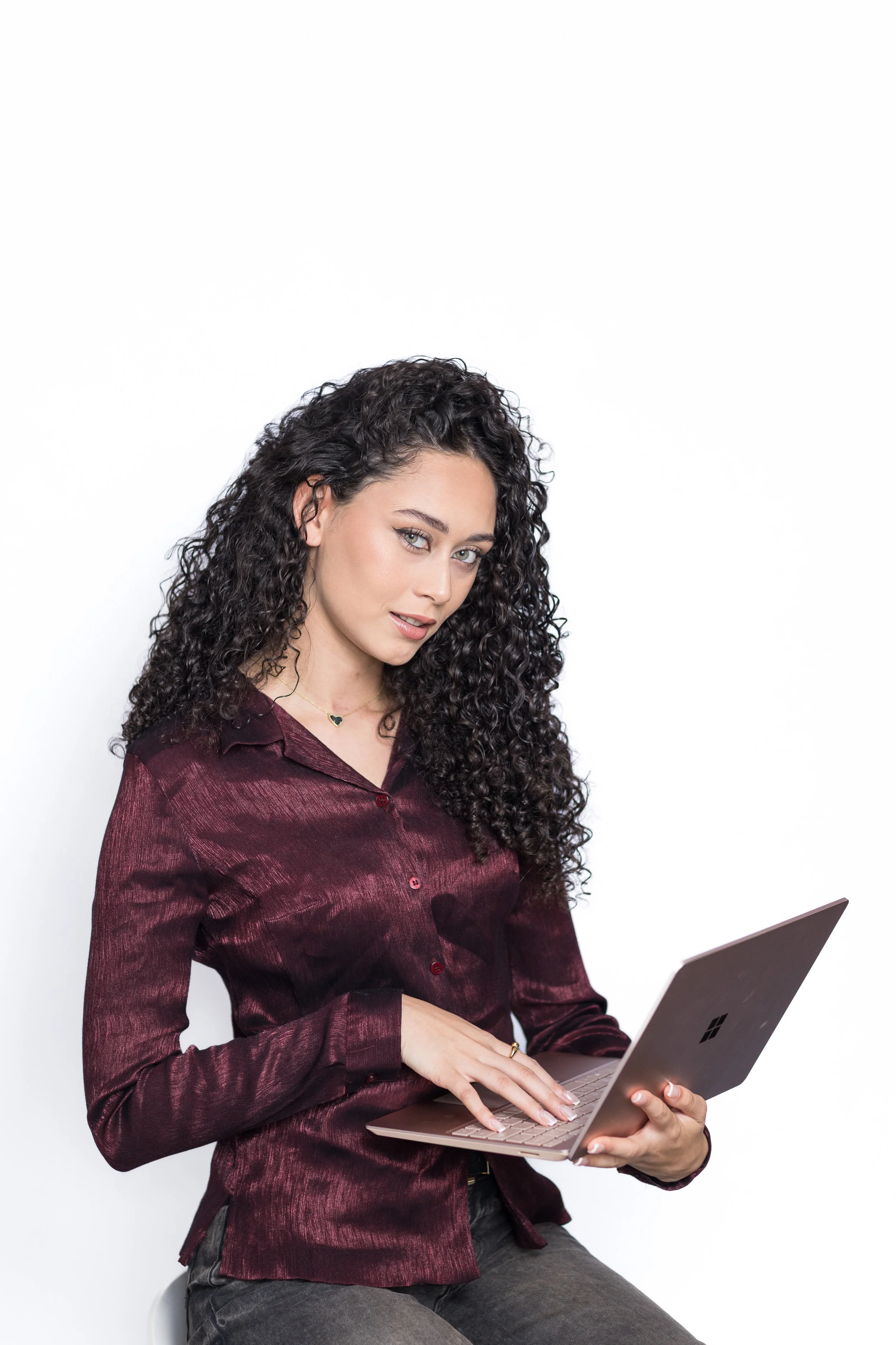 Young woman with curly hair using a Microsoft Surface laptop against a white background