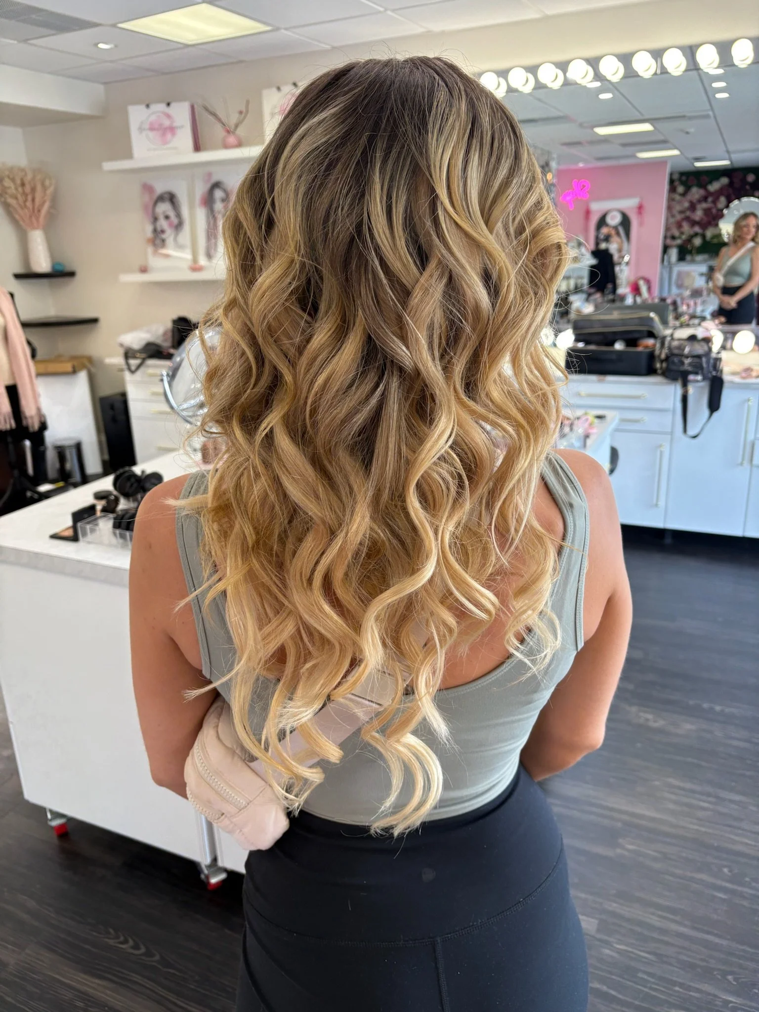 Woman with long, blonde, wavy hair in a salon, facing away.