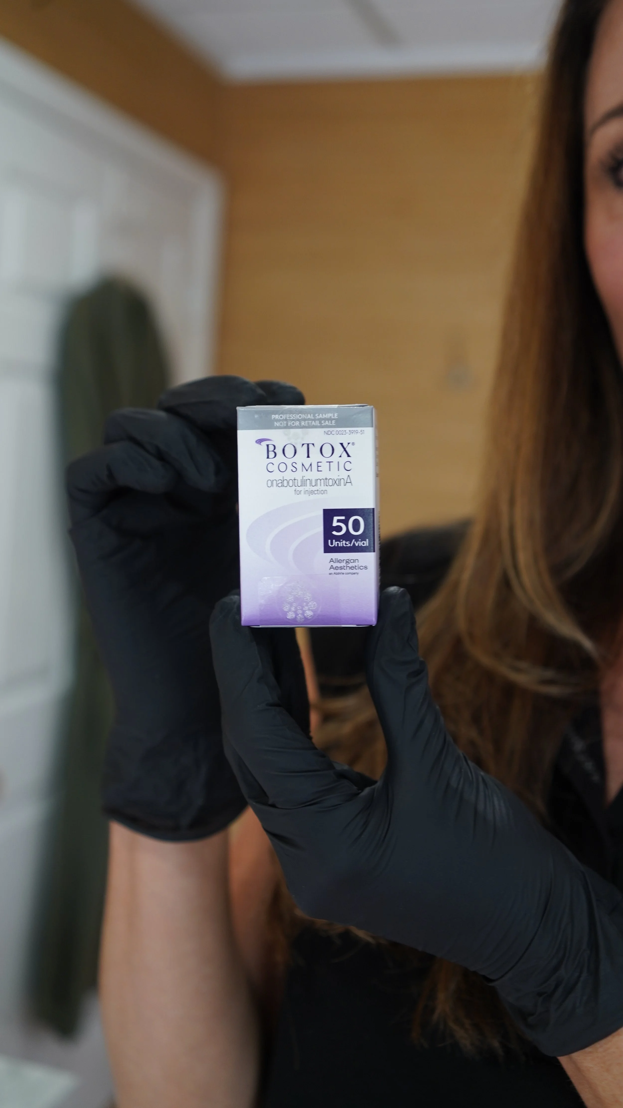 A woman is lying down with her eyes closed while receiving a cosmetic treatment with a syringe, likely for facial injection or Botox.