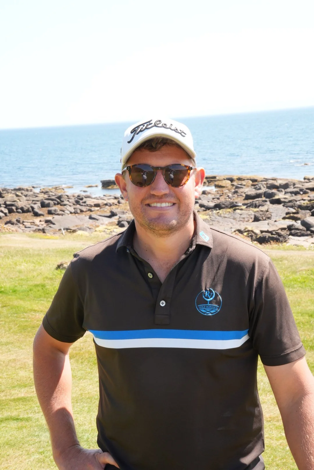 Golf coach in a striped polo shirt, white cap and sunglasses beside the coast