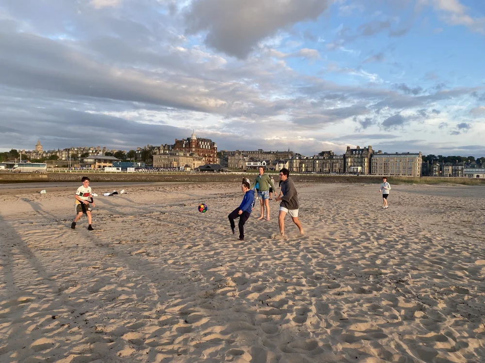 Junior campers playing football on a sandy beach
