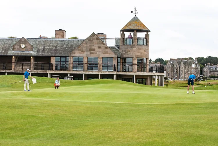 Junior golfers on a putting green beside a clubhouse with a tower