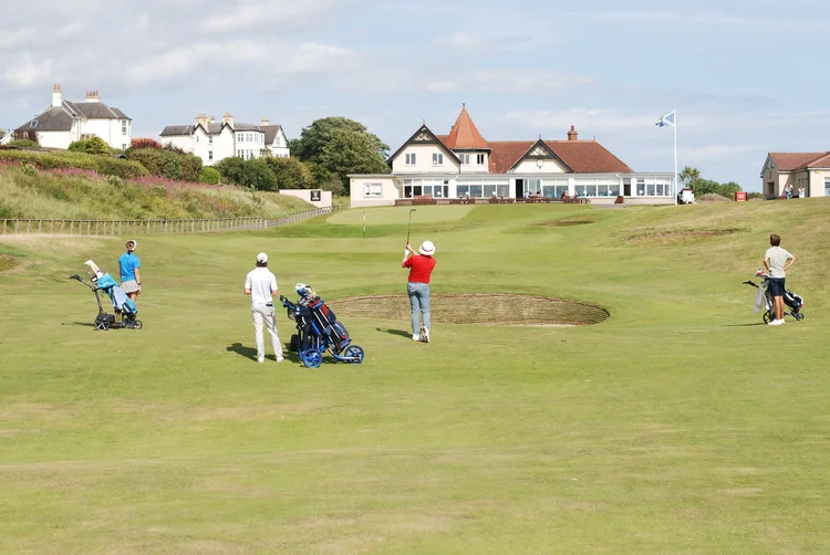 Junior golfers practising on a green with a clubhouse in the background