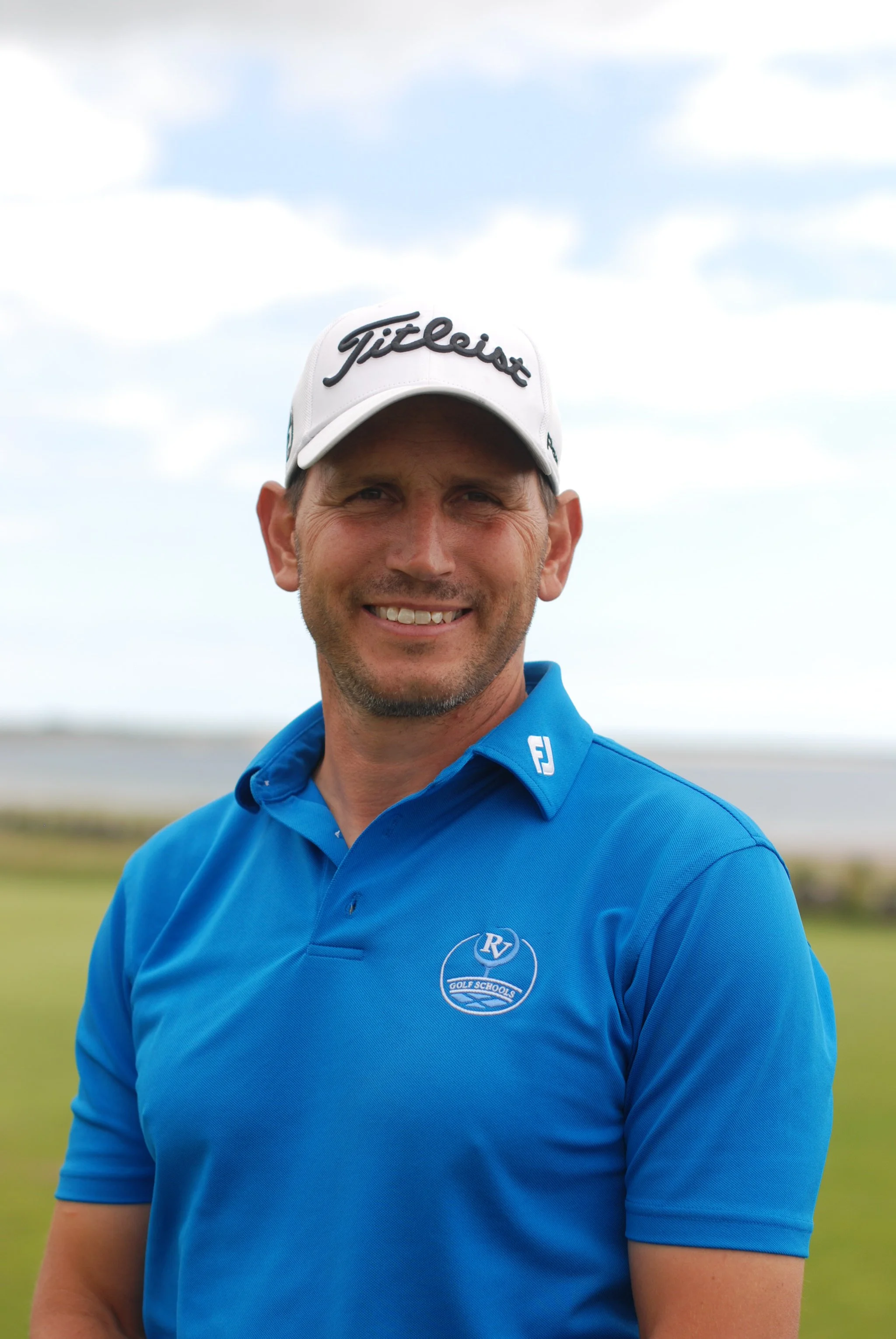 Golf coach wearing a blue polo shirt and white cap on a golf course