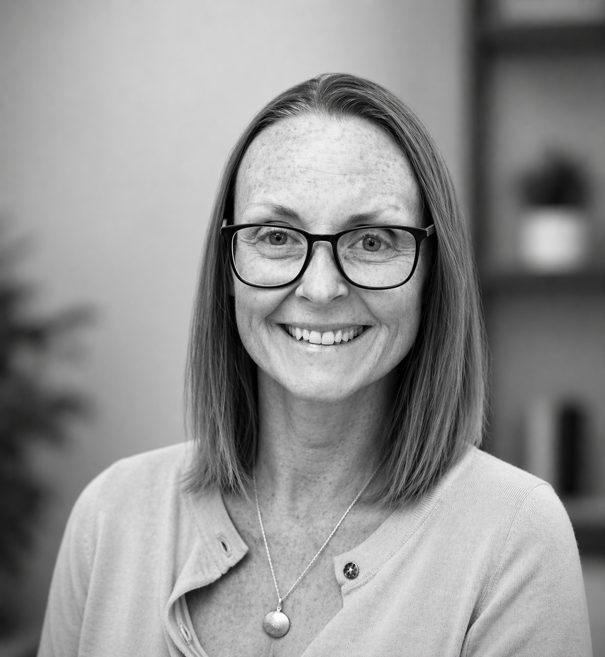 Team headshot of a woman with glasses and long hair taking a selfie style, black and white photo.
