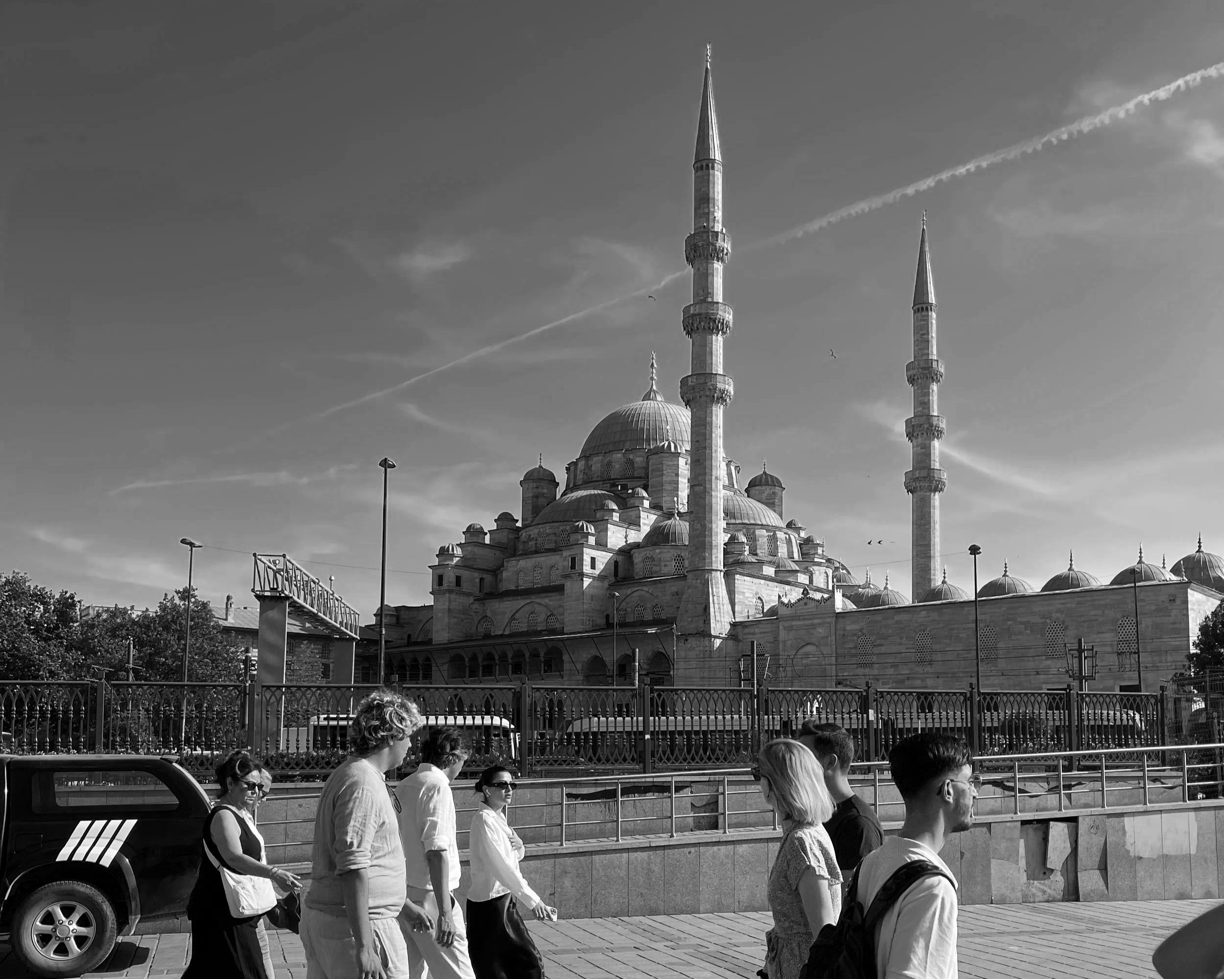 A group of people walking past a fence with a mosque with two minarets in the background.