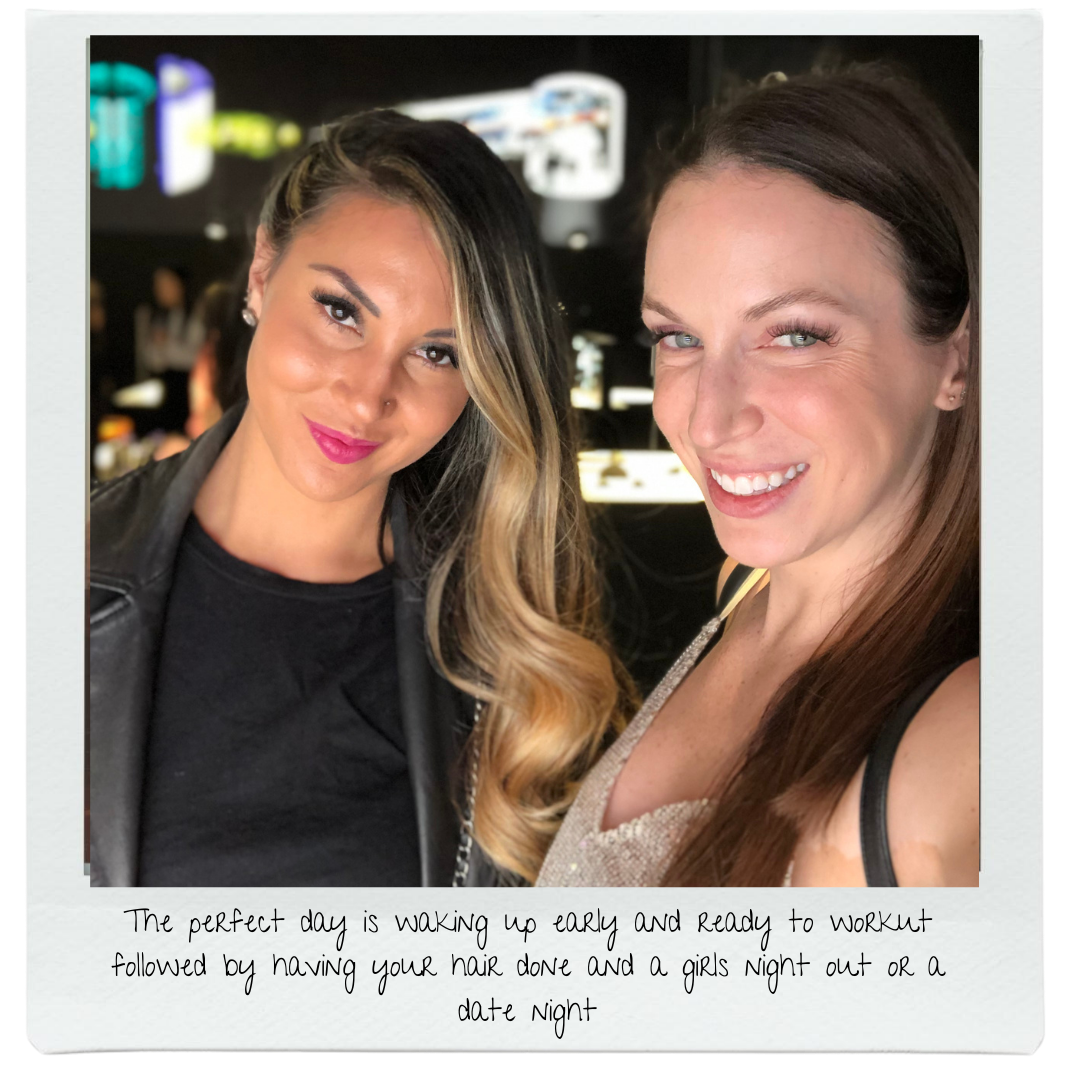 Two women smiling and taking a selfie in a dark indoor setting, with bright lights and blurred background.