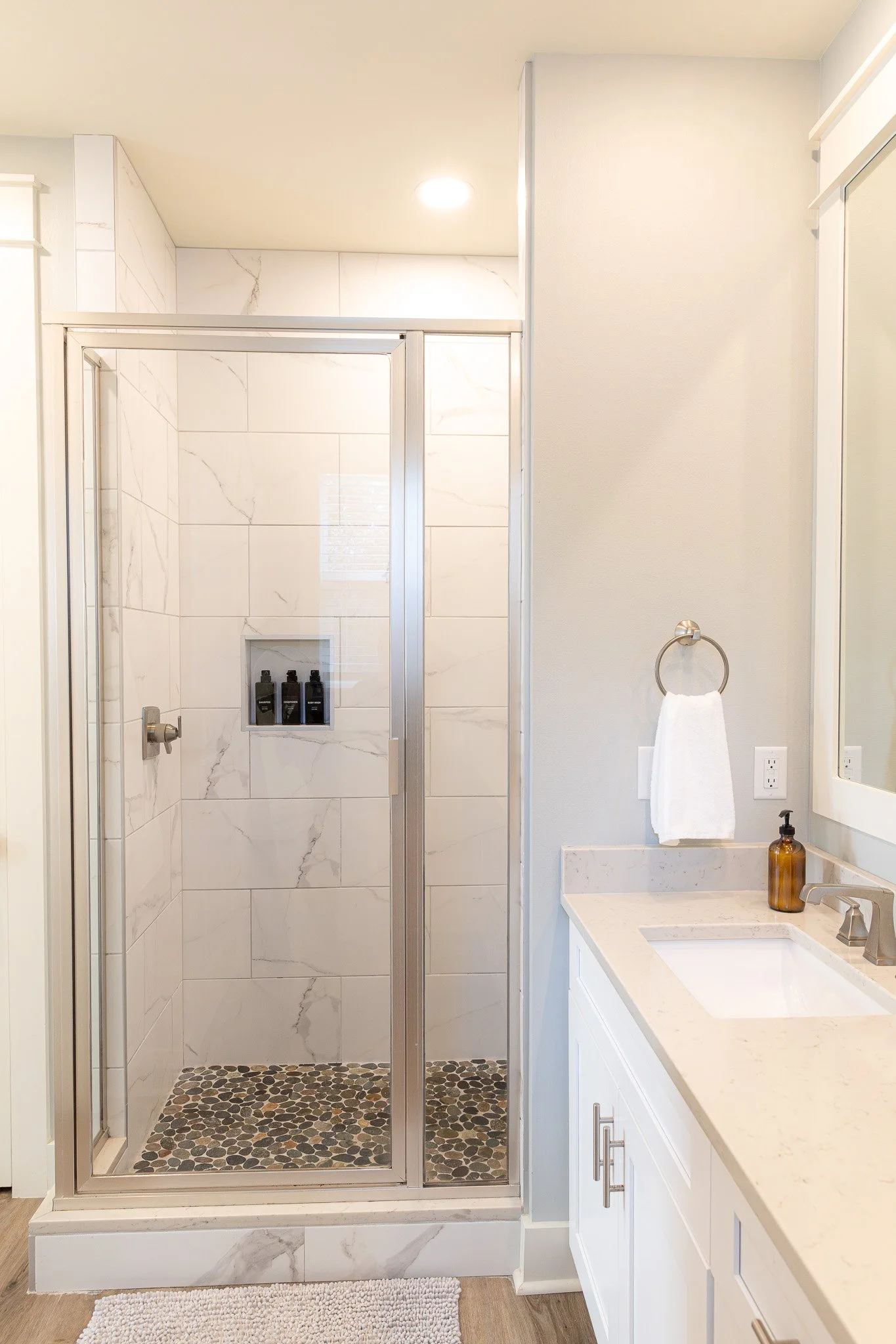 Bathroom with a glass shower enclosure, marble tiles, a white vanity with a single sink, a mirror, and a towel hanging on a ring.