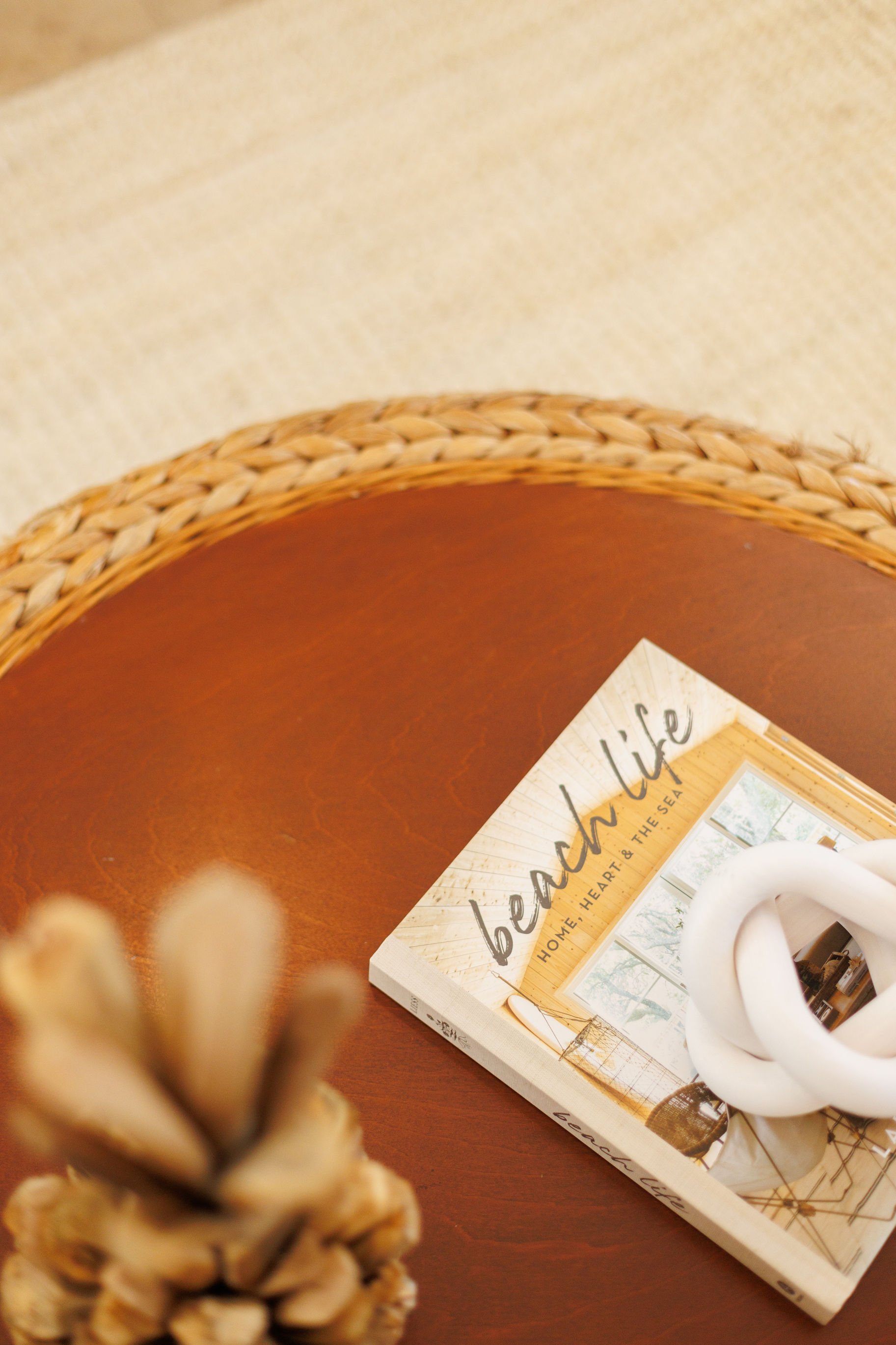 A table with a book titled 'Beach Life' and a white decorative knot. A pineapple is partially visible at the bottom left corner.