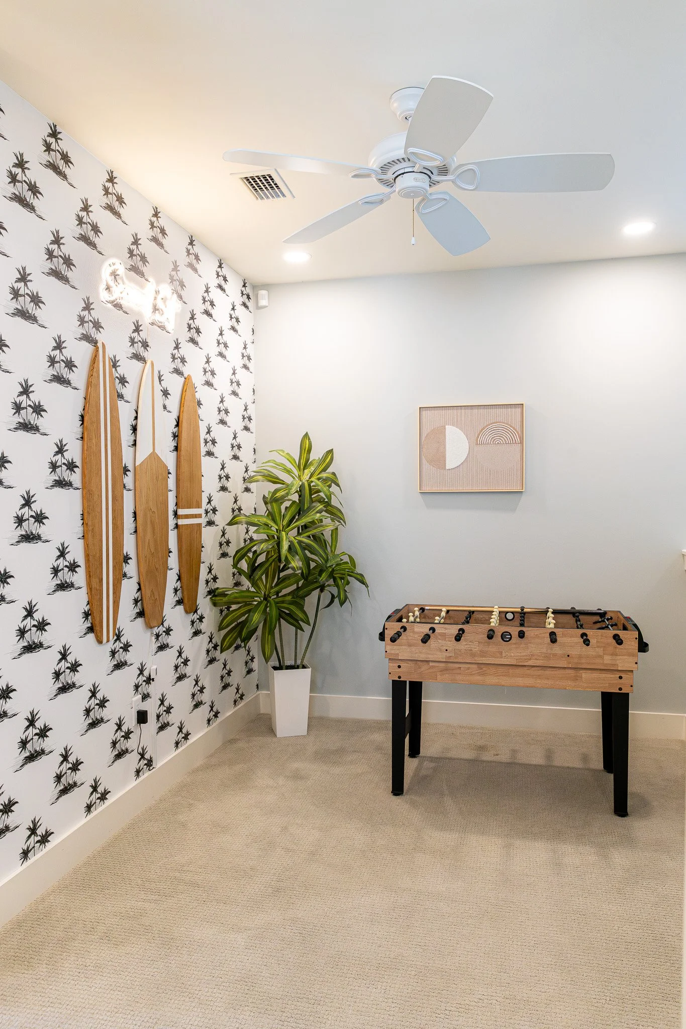 Another view of the Salty Surf game room with tropical palm wallpaper, surfboard decor, foosball table, and coastal artwork.