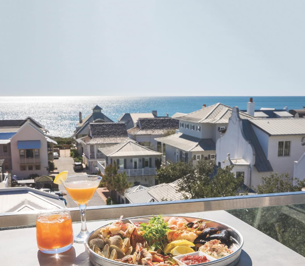 Collage of three images: a decorated dining room with table set for a meal, a balcony with a view of rooftops and the ocean, and a close-up of bread with dipping sauce.