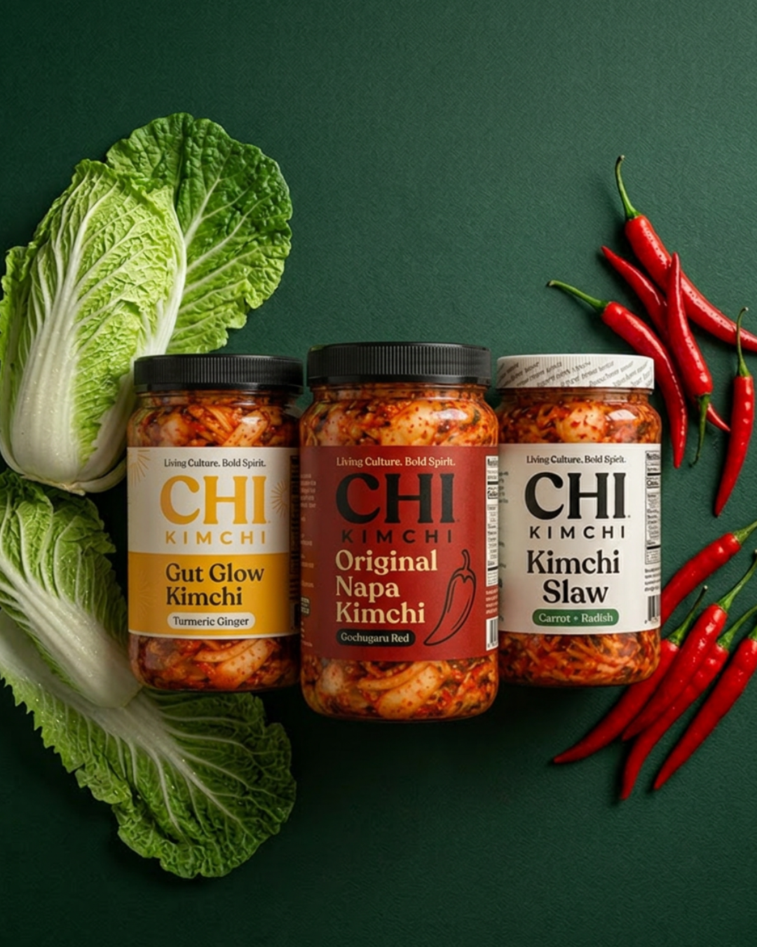 Three jars of Kimchi from Chi Kimchi brand with napa cabbage and red chili peppers on a green background.