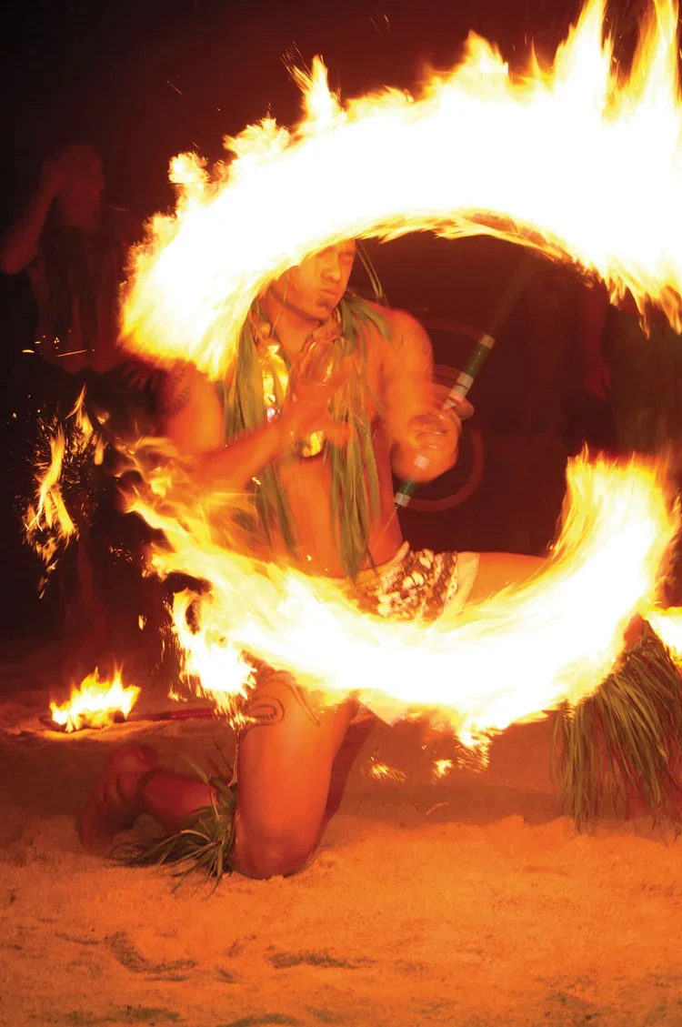 A performer kneeling on the ground and spinning a flaming poi, creating a circle of fire during a night fire performance.