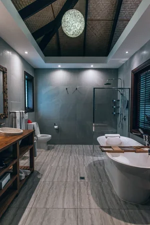 Modern bathroom with a walk-in shower, bathtub, toilet, and wooden vanity, illuminated by ceiling lights and natural light from windows.