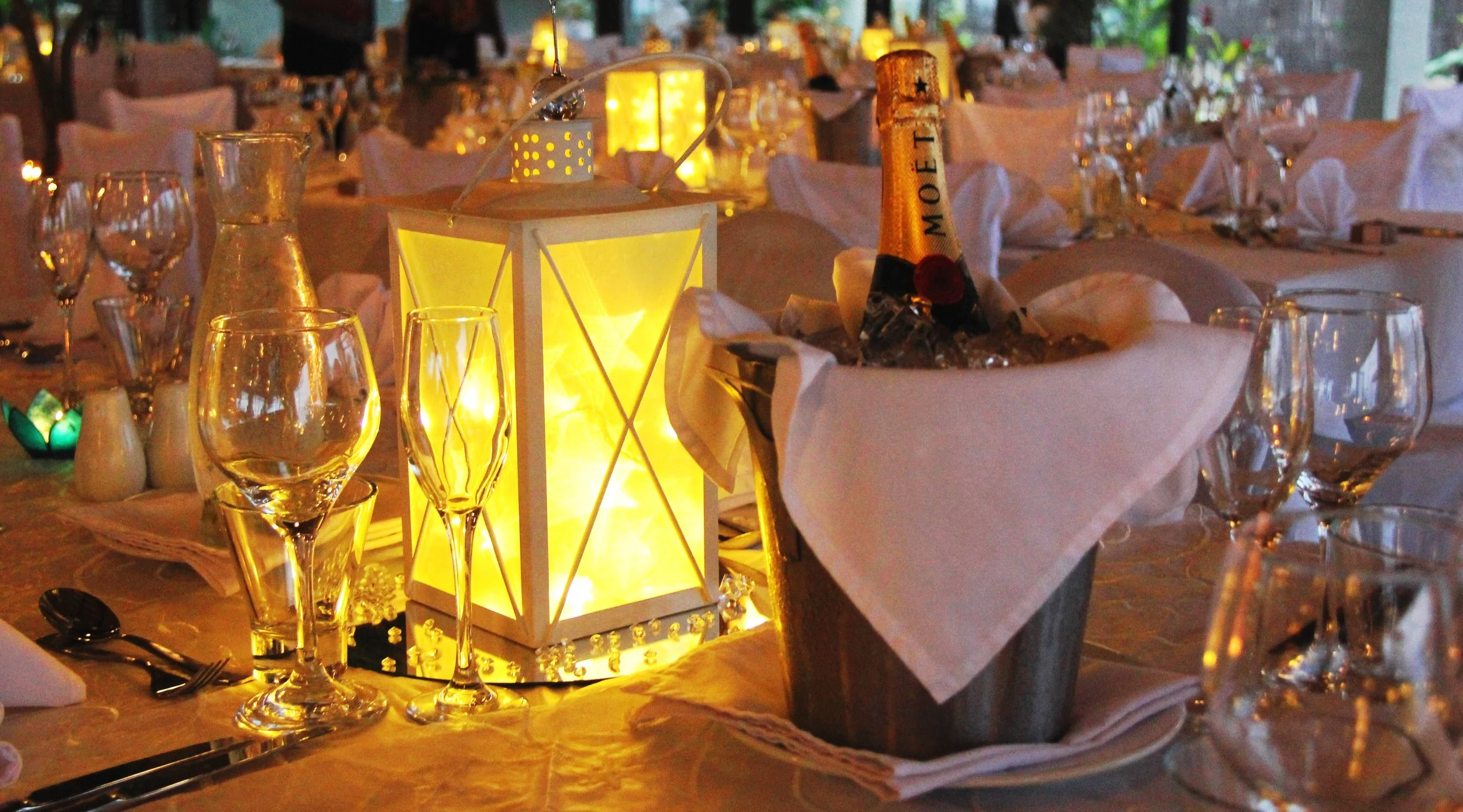 A decorated banquet table with wine glasses, a lantern, and a bottle of champagne in an ice bucket, set for a celebration or formal event.