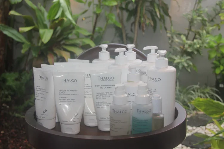 Collection of Thalgo skincare products, including face masks and lotions, on a black stand outdoors with green foliage in the background.