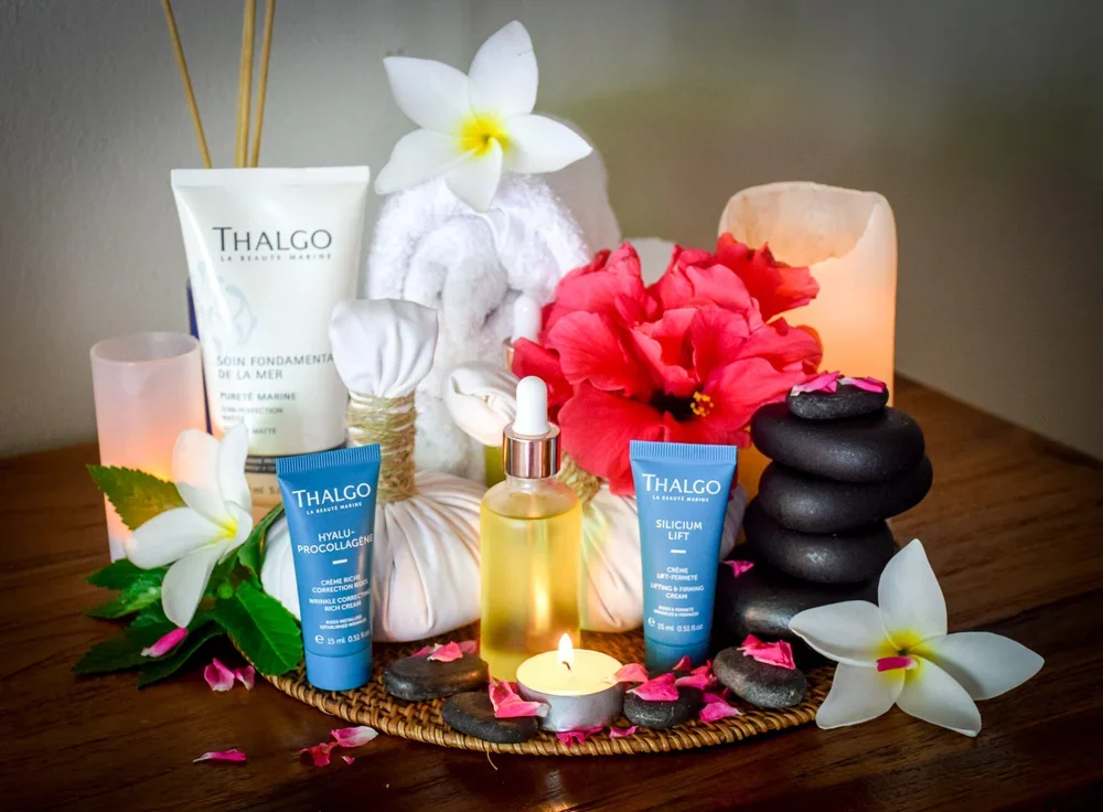 Spa setting with skincare products, candles, flowers, and stones on a wooden surface.