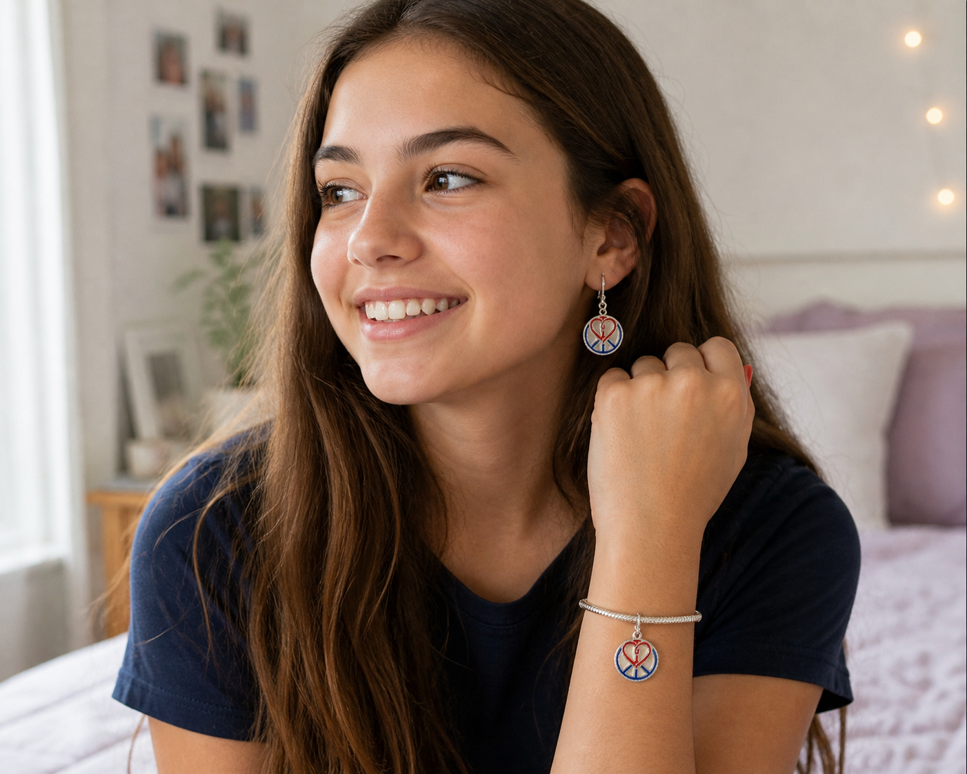 A young woman with long brown hair is smiling and looking to her left. She is wearing peace sign jewelry, including earrings, a bracelet, and a necklace, all with red, white, and blue colors. The background appears to be a cozy bedroom with photos on the wall and soft lighting.