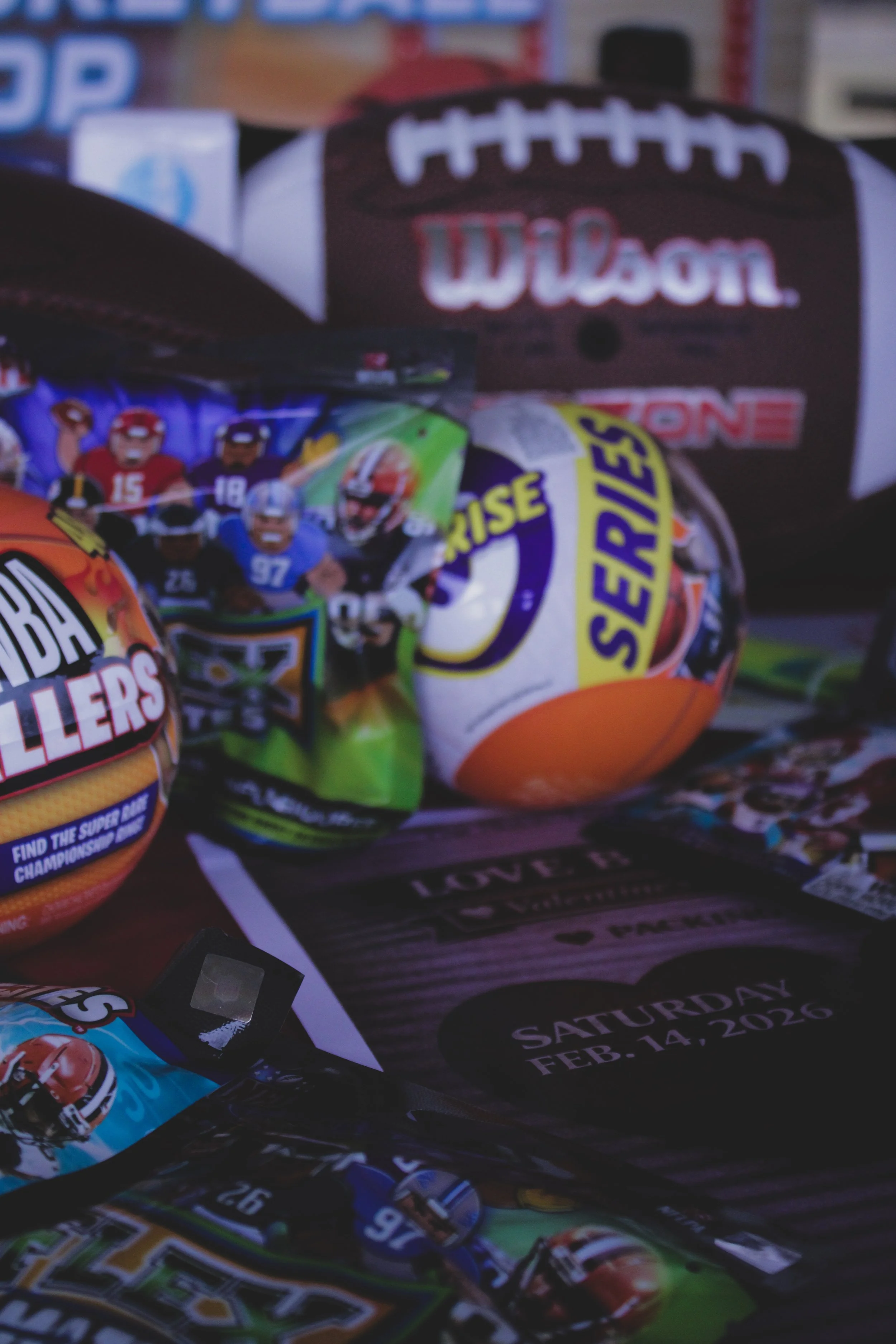 A collection of colorful squishy rubber stress balls with cartoon characters and sports themes, laid out on a surface, with a card indicating an event date of February 14, 2026.