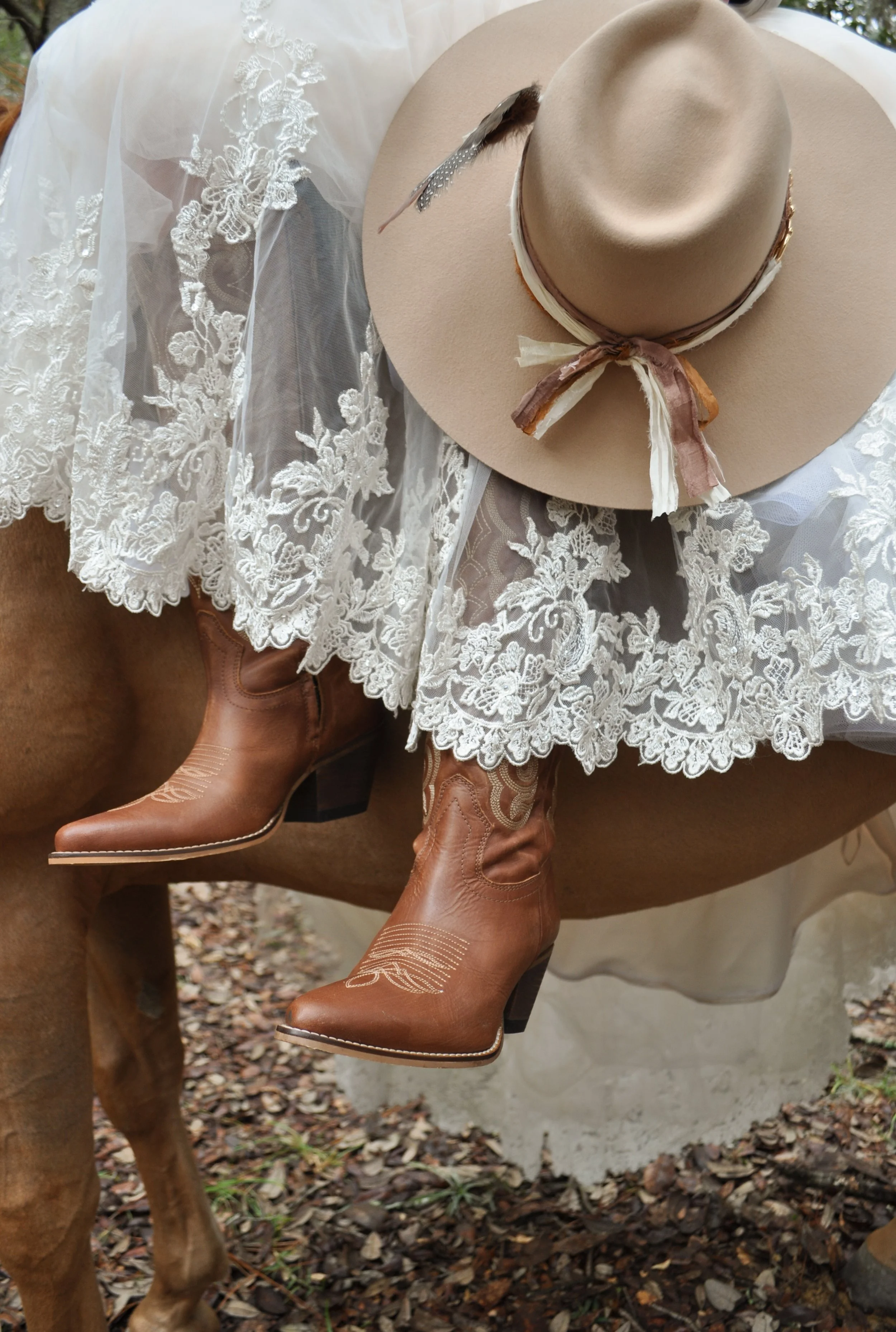 An outdoor dining setup with wooden tables and chairs, decorated with floral centerpieces, on a grassy yard during sunset, with a rustic barn in the background and string lights hanging from the barn to the trees.