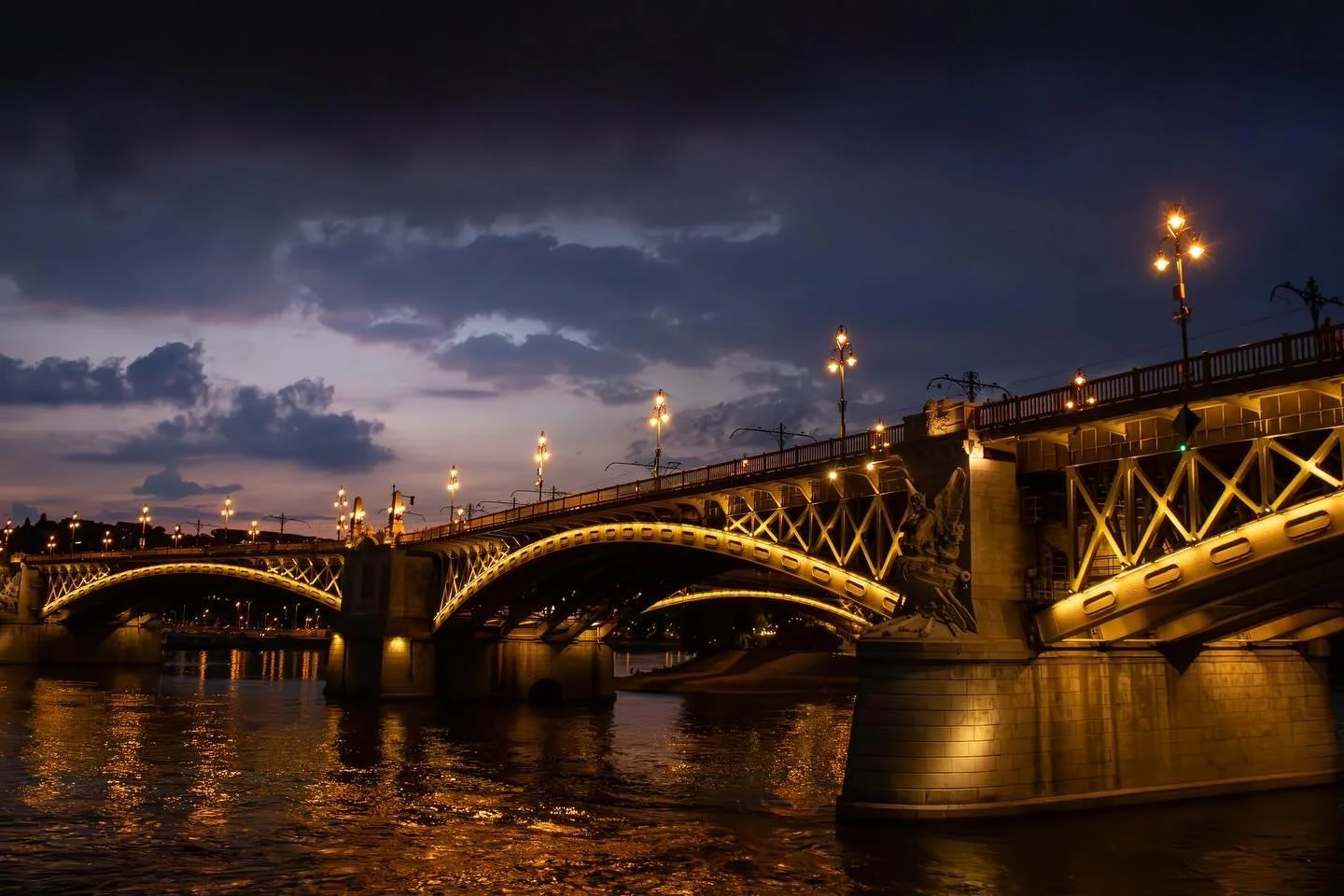 Margit h&iacute;d bridge Budapest - during golden hour, dark clouds fill the sky as a thunder erupts nearby. The lights provide a clear colour scheme of gold that mimics the sunset accompanied by a lush deep blue from the clouds.