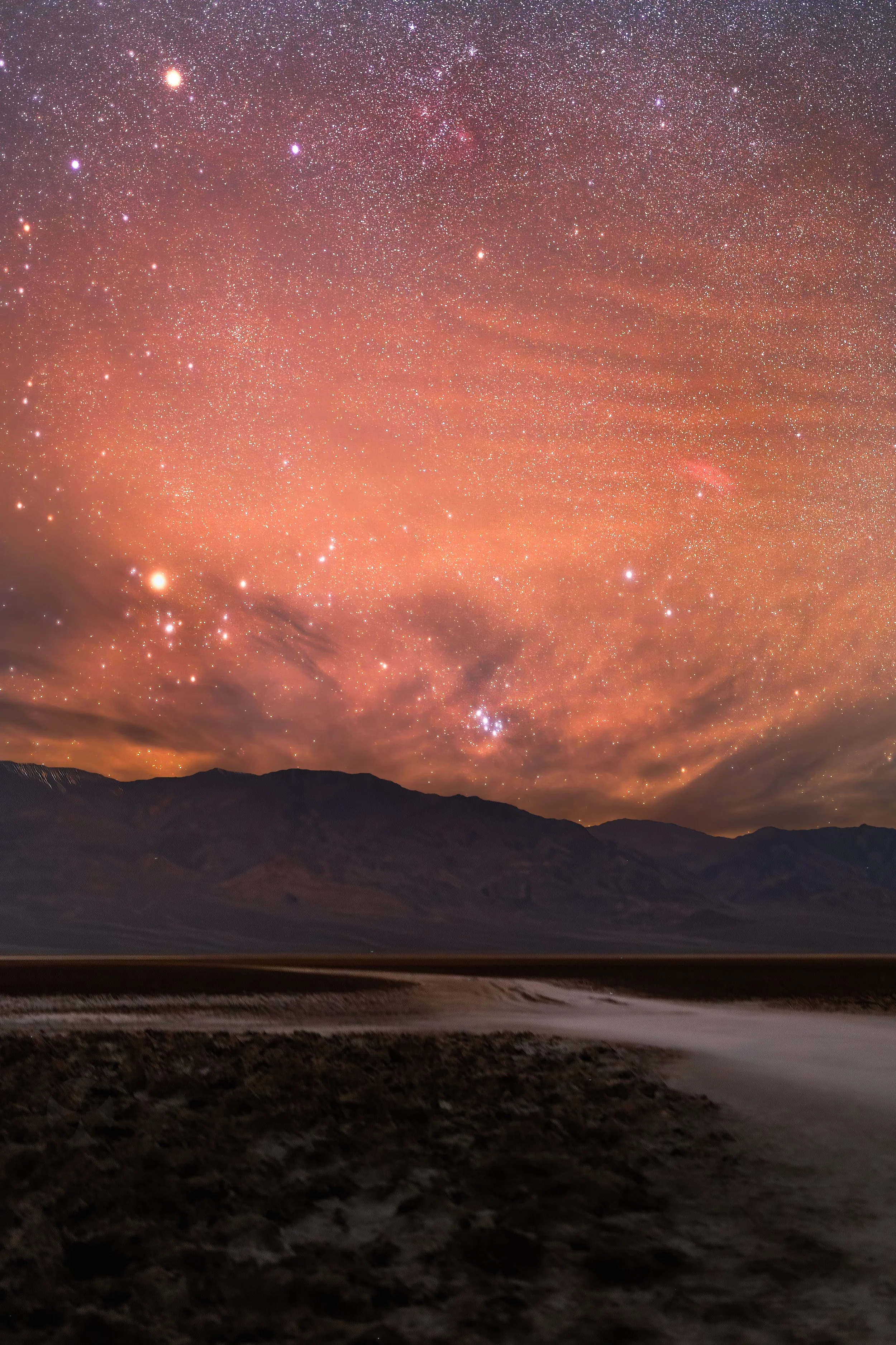 Night sky filled with stars over mountains and a rugged terrain. Death valley