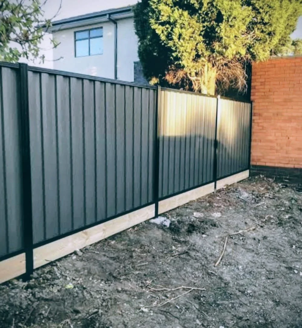 Metal fence next to a brick wall with a house and trees in the background.