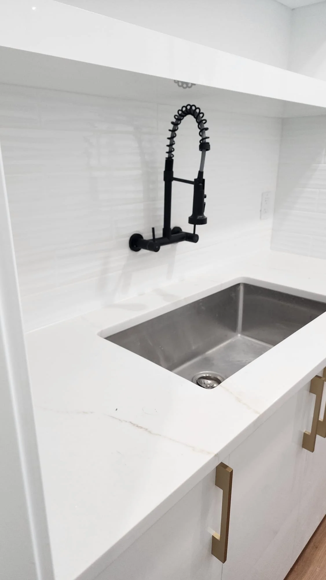 Modern kitchen sink with black flexible faucet on white countertop.