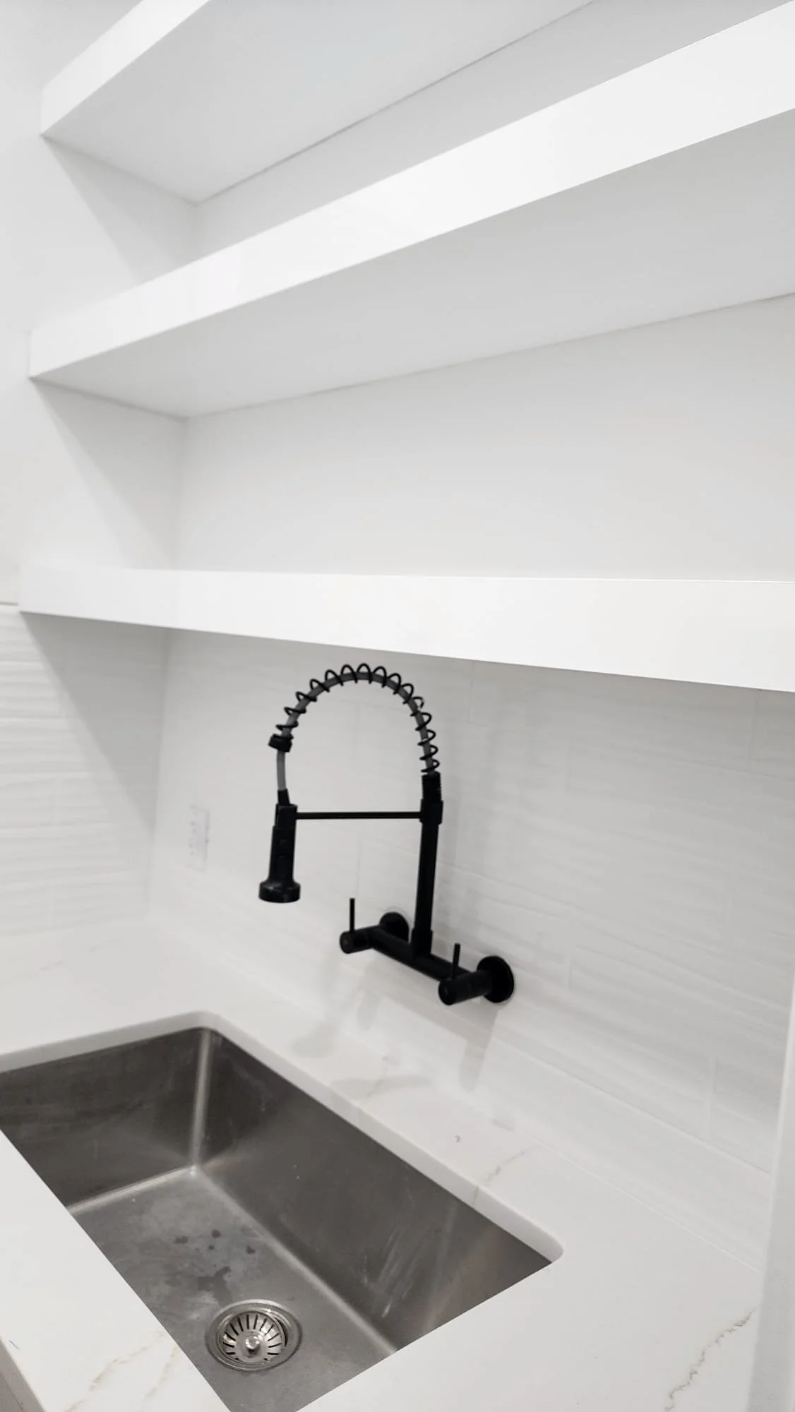 A modern kitchen sink with a black pull-down faucet and white countertops.