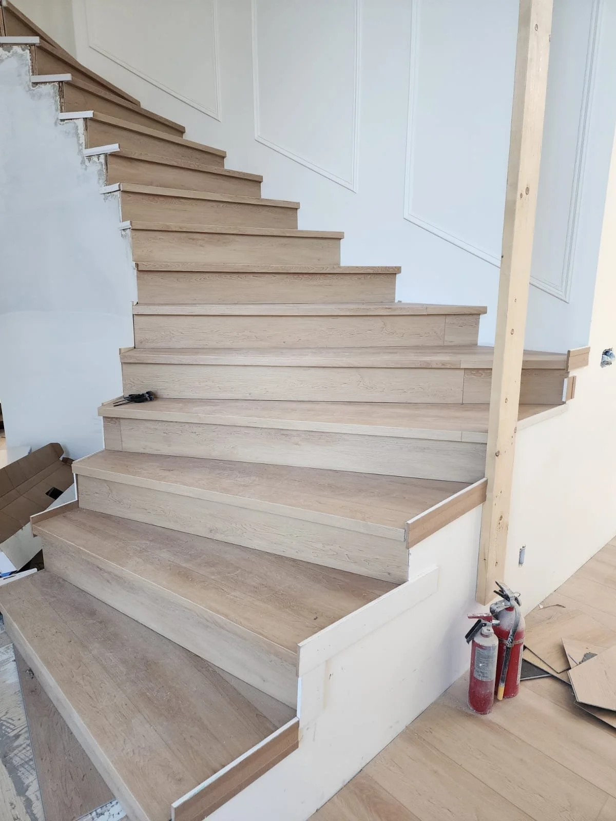 Under construction wooden staircase with unfinished steps and stairs, fire extinguishers, and construction materials around.