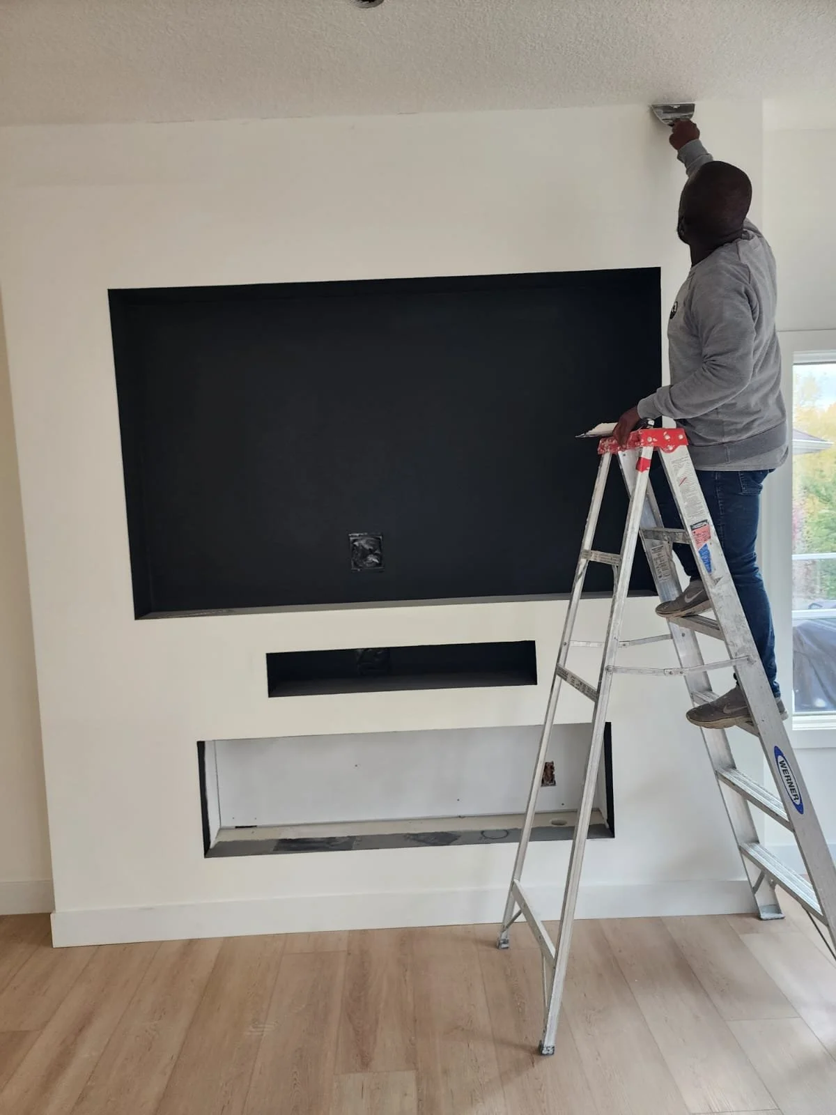 A person standing on a ladder painting the ceiling of a room.