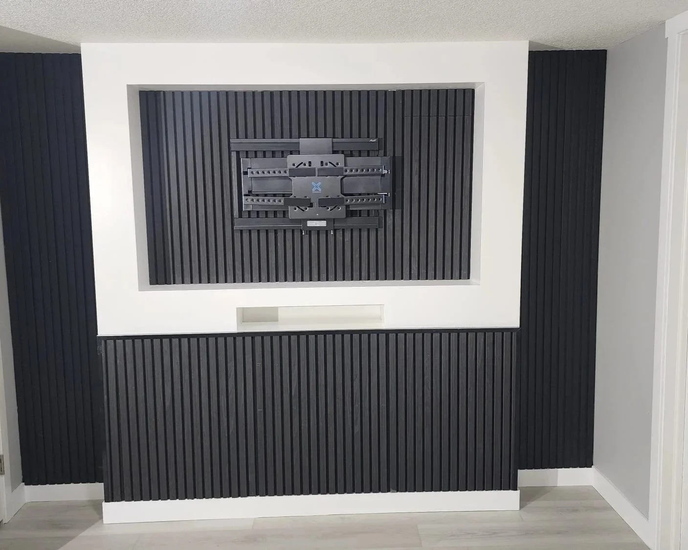A television mount on a black slatted wall with a white frame. The mount is empty, with no TV attached.