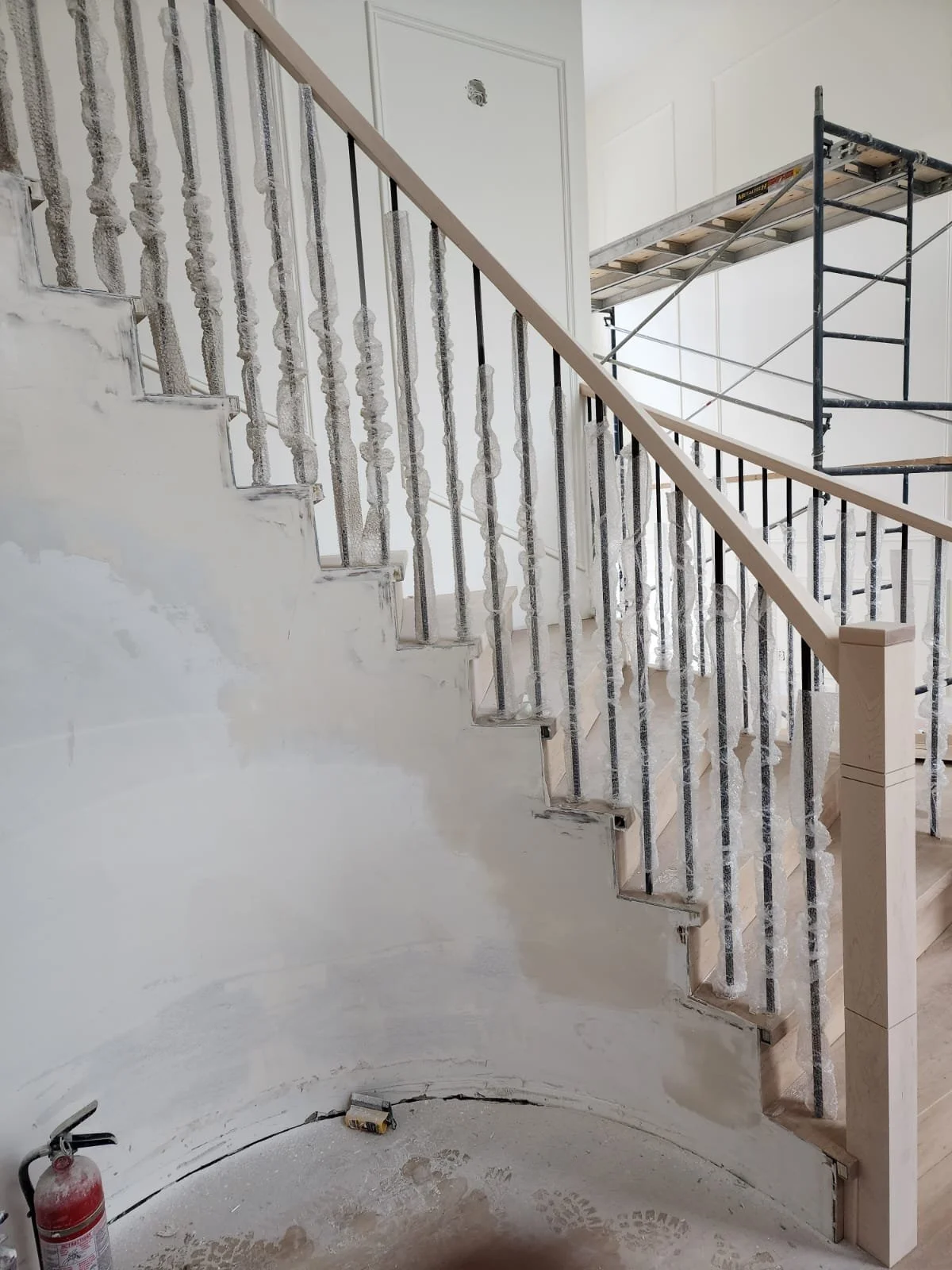 Interior of a staircase under construction with a fire extinguisher on the floor and scaffolding in the background.