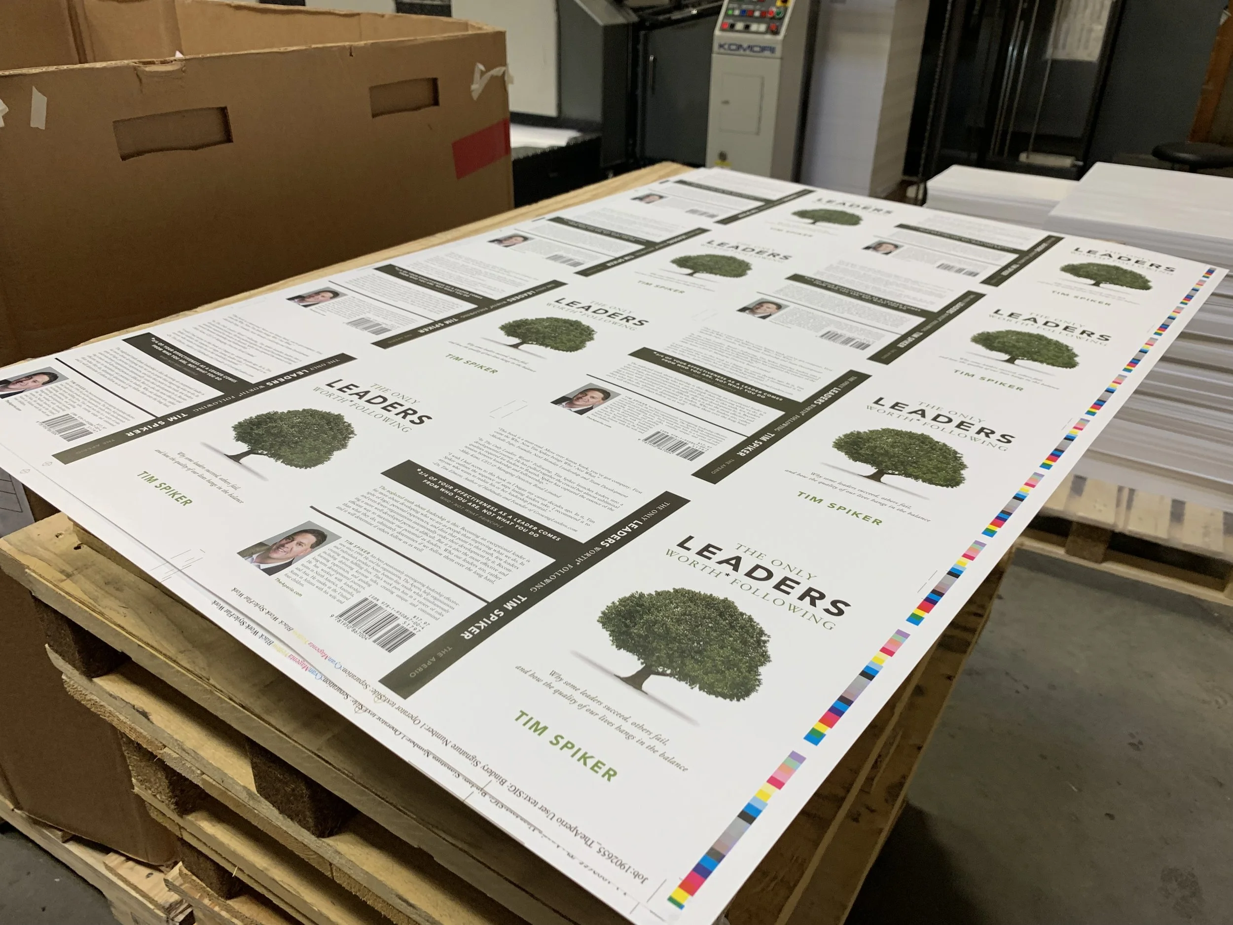 Printed flyers or posters with a tree illustration, text about leadership and following, and a photograph of a man, all laid out on a workbench in an industrial or printing environment.