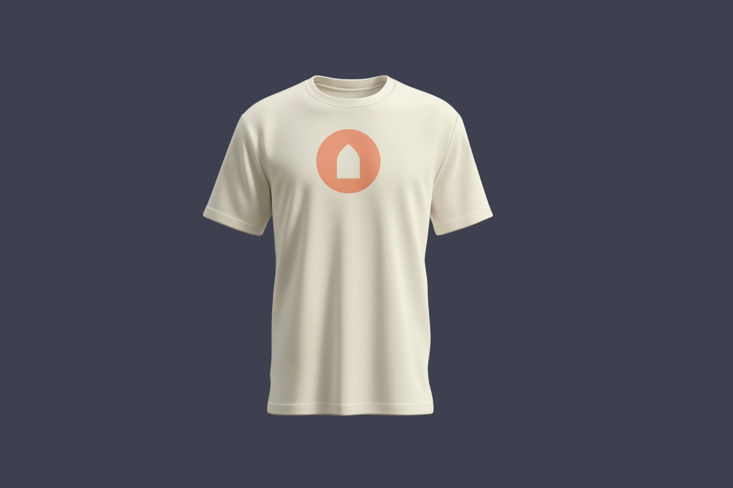 Cream-colored T-shirt with a circular logo featuring a house silhouette in orange on the front, displayed against a dark background.