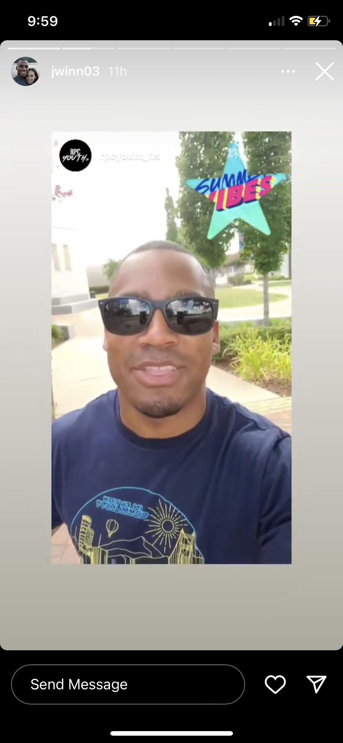 A man wearing sunglasses and a dark T-shirt, standing outdoors on a sunny day, with a sticker that says 'SUMMER VIBES' in colorful font and a green star background.