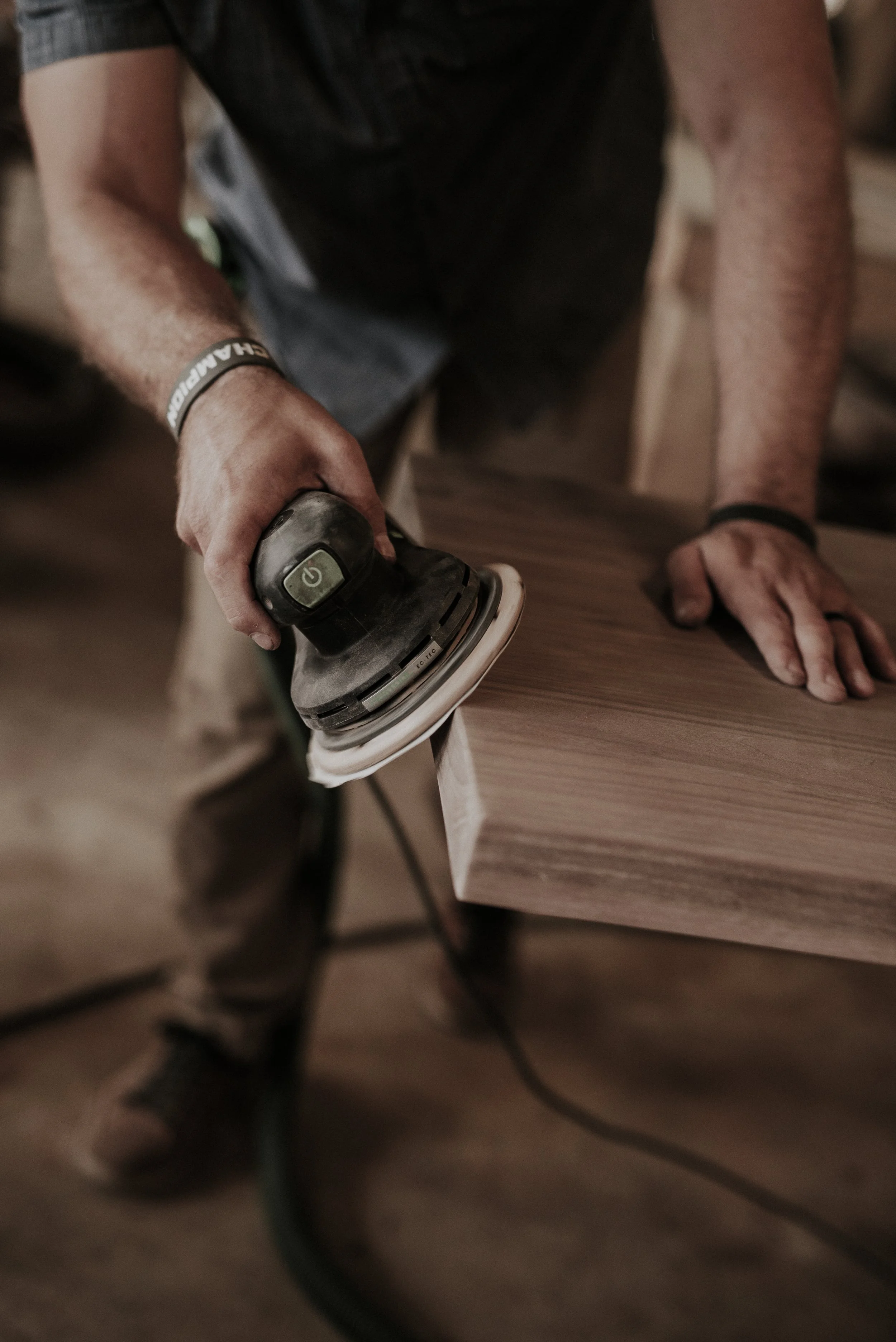 Person sanding a wooden surface with an electric sander.