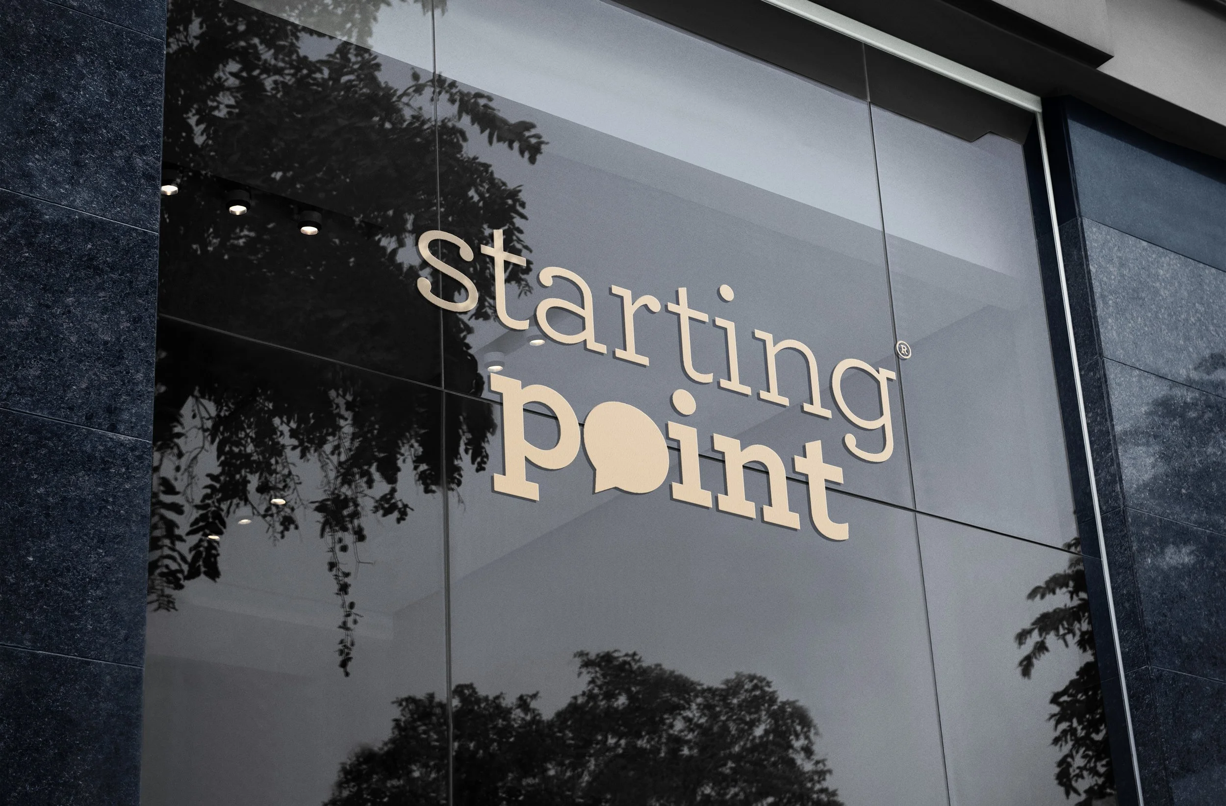 Reflection of trees on glass window with Starting Point logo on building exterior.