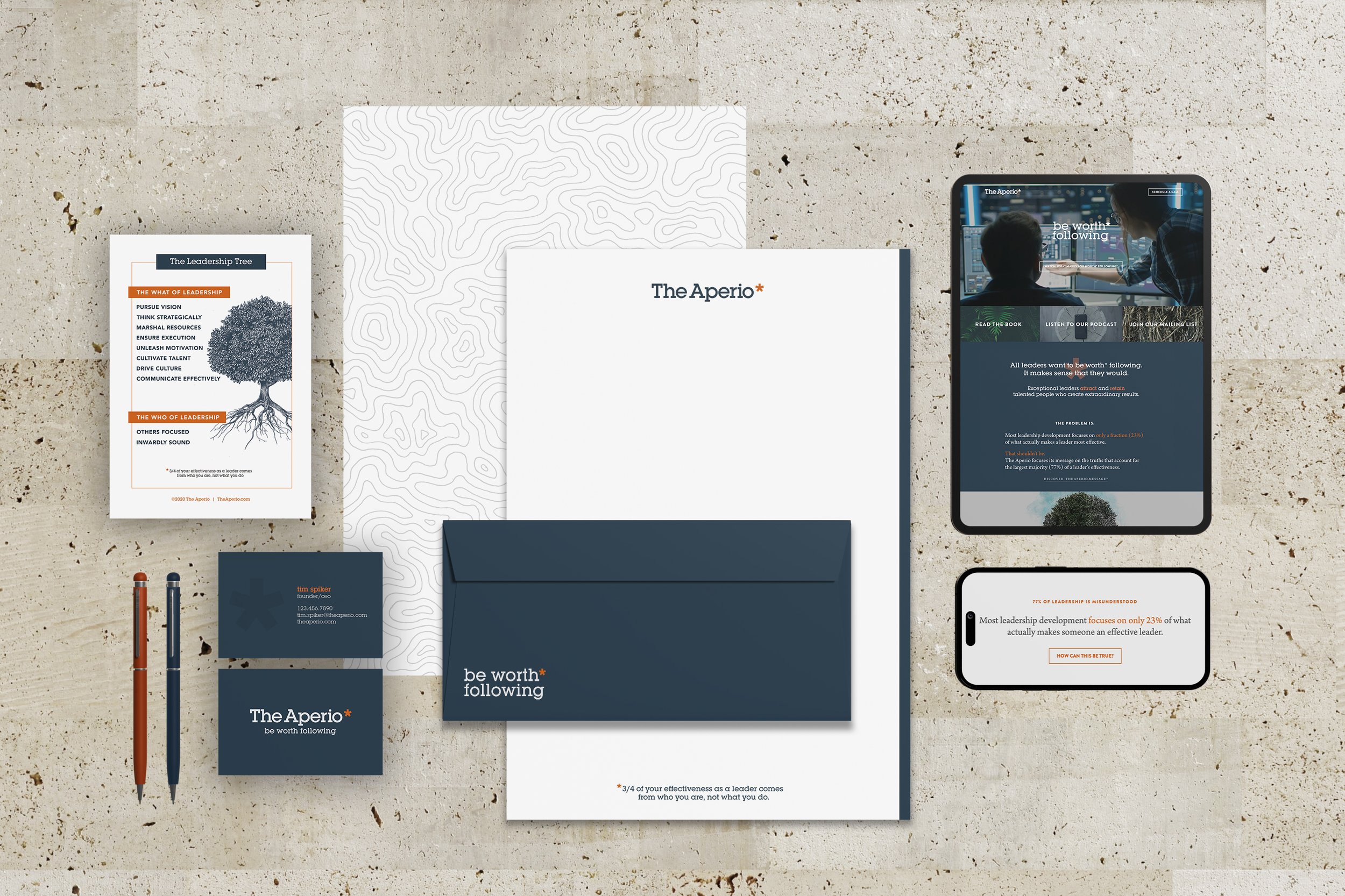A collection of branding and stationery items for The Aperio, including flyers, business cards, pens, a folder, a tablet displaying a website, and a smartphone, all placed on a textured surface.